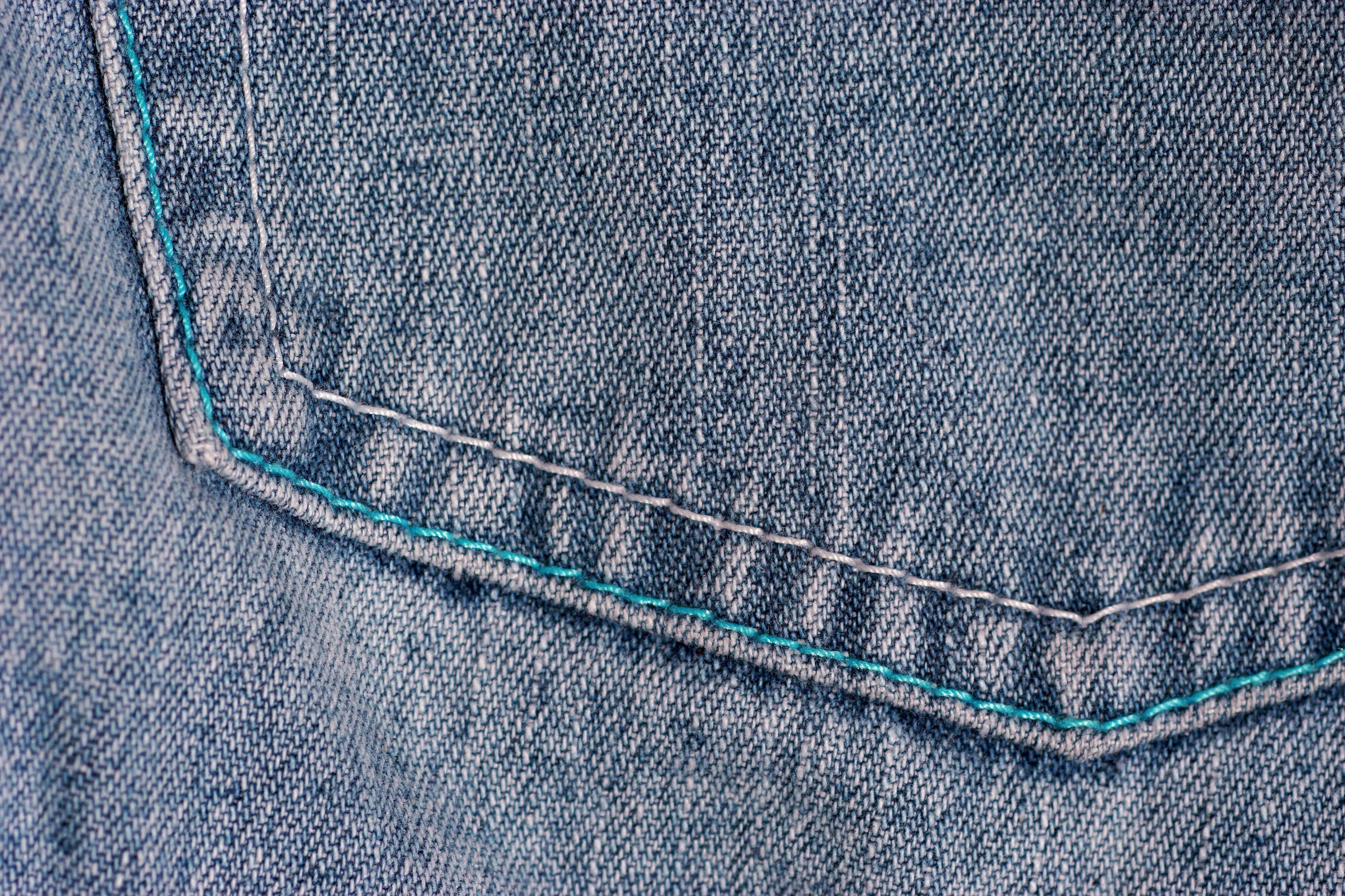 Denim 桌布 壁紙 — 牛仔布口袋特寫，帶有對比的青綠色和白色縫線，突顯出紋理織物編織。