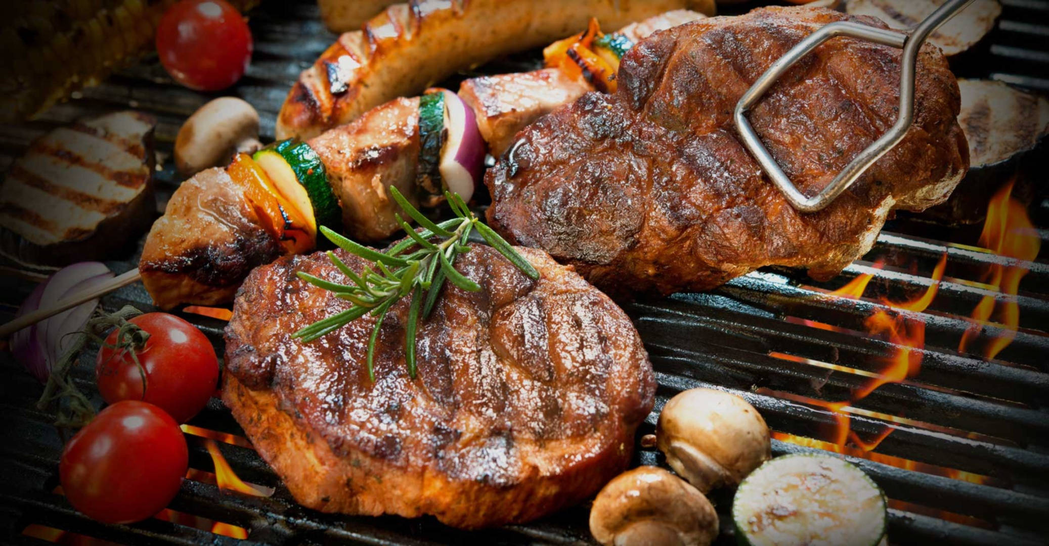 meat 桌布 壁紙 — 牛排和串燒在火焰上烤得滋滋作響，周圍有迷迭香、番茄和蘑菇。