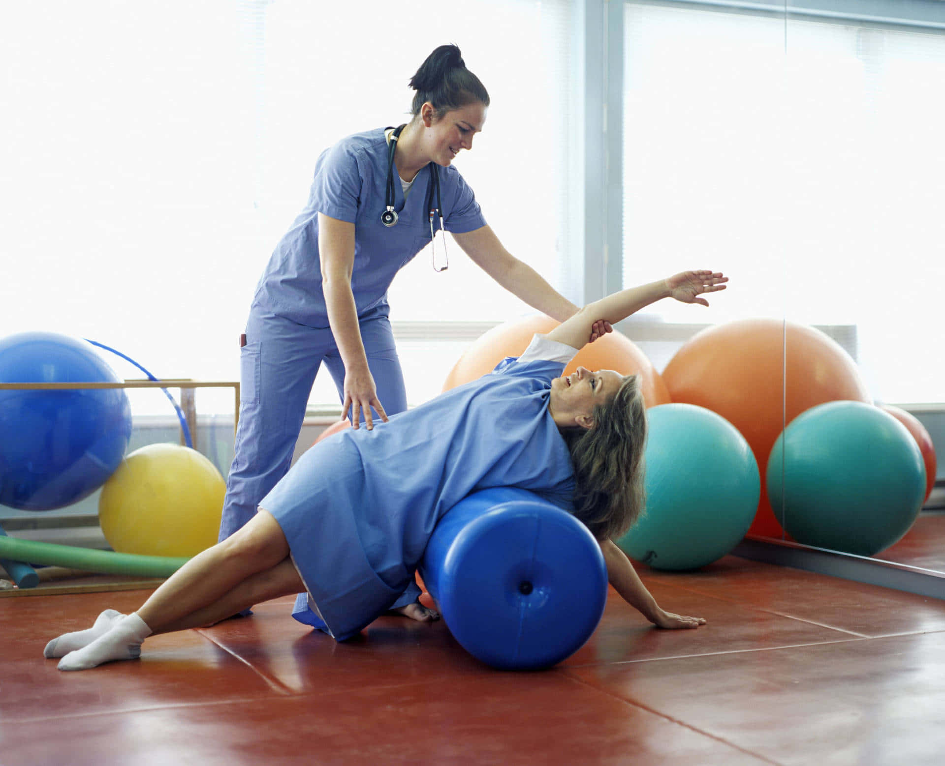 Exercise 桌布 壁紙 — 物理治療師在明亮的治療室中協助患者於藍色穩定性球上進行核心運動。