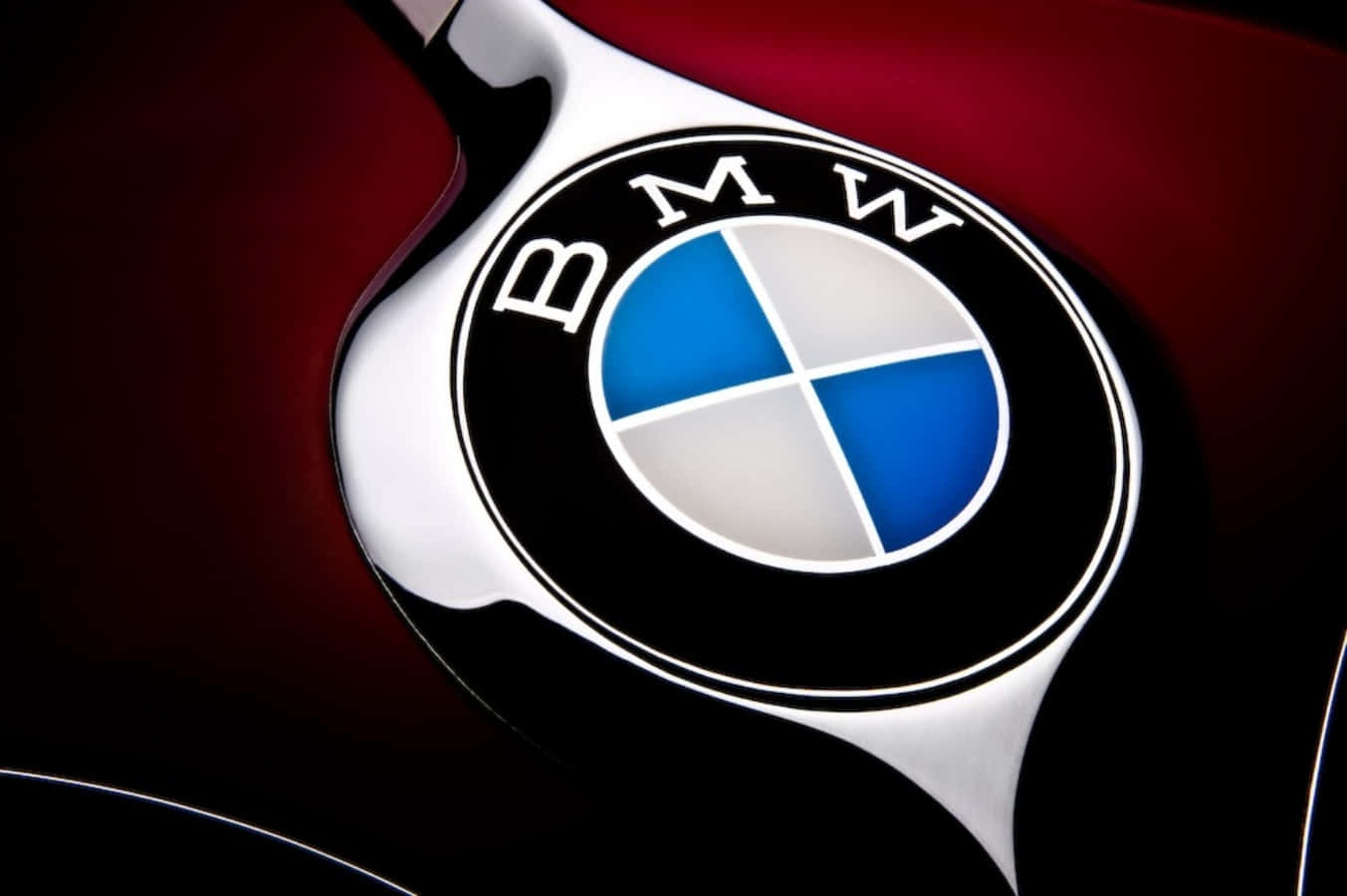 Bmw Logo 桌布 壁紙 — 特寫：在戲劇性燈光下，深紅色引擎蓋上閃亮的BMW標誌。