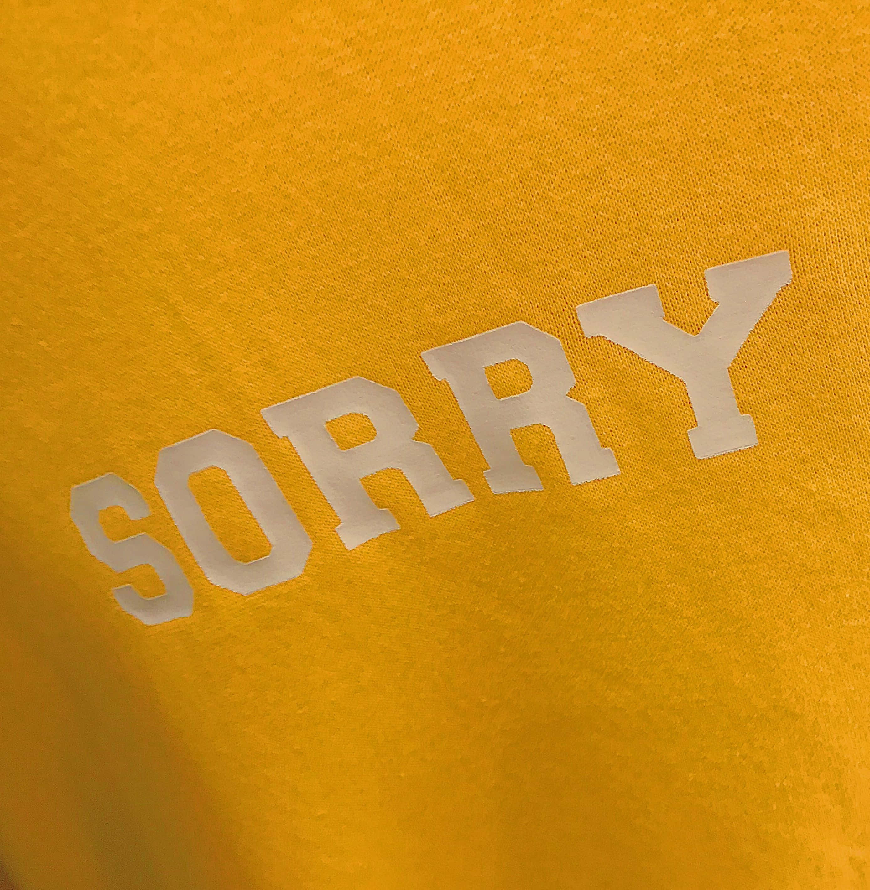 text 桌布 壁紙 — 特寫：帶有紋理的金黃色布料上，白色粗體「SORRY」文字，光線柔和。