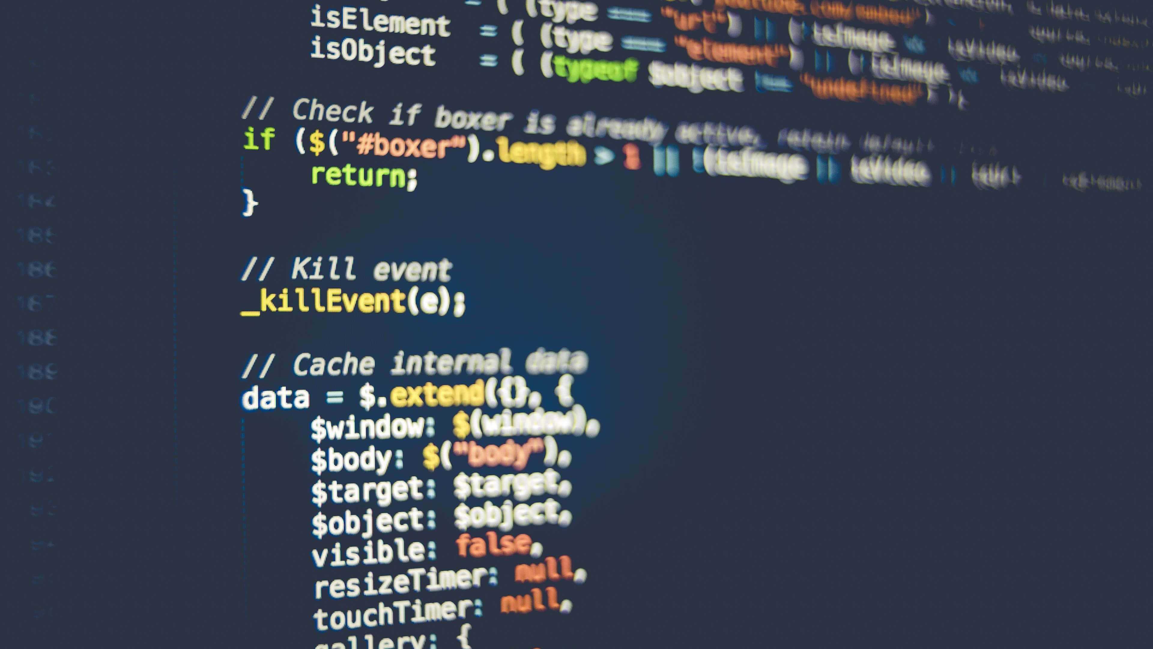 It Computer 桌布 壁紙 — 特寫：暗色螢幕上發光的彩色程式碼行，帶模糊的語法高亮。