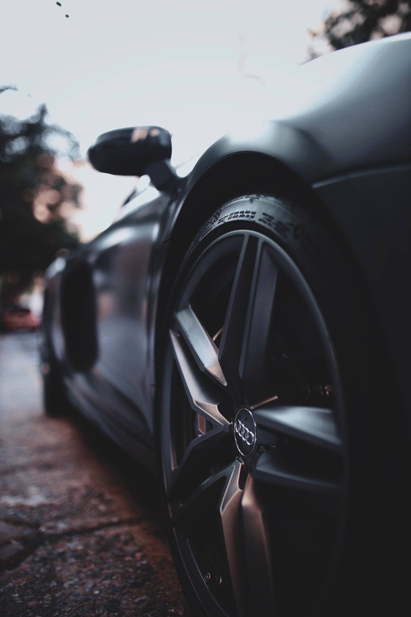 Luxury 桌布 壁紙 — 特寫：暮色中濕滑街道上，一輛時尚消光黑色奧迪跑車的車輪，背景是模糊的樹木。