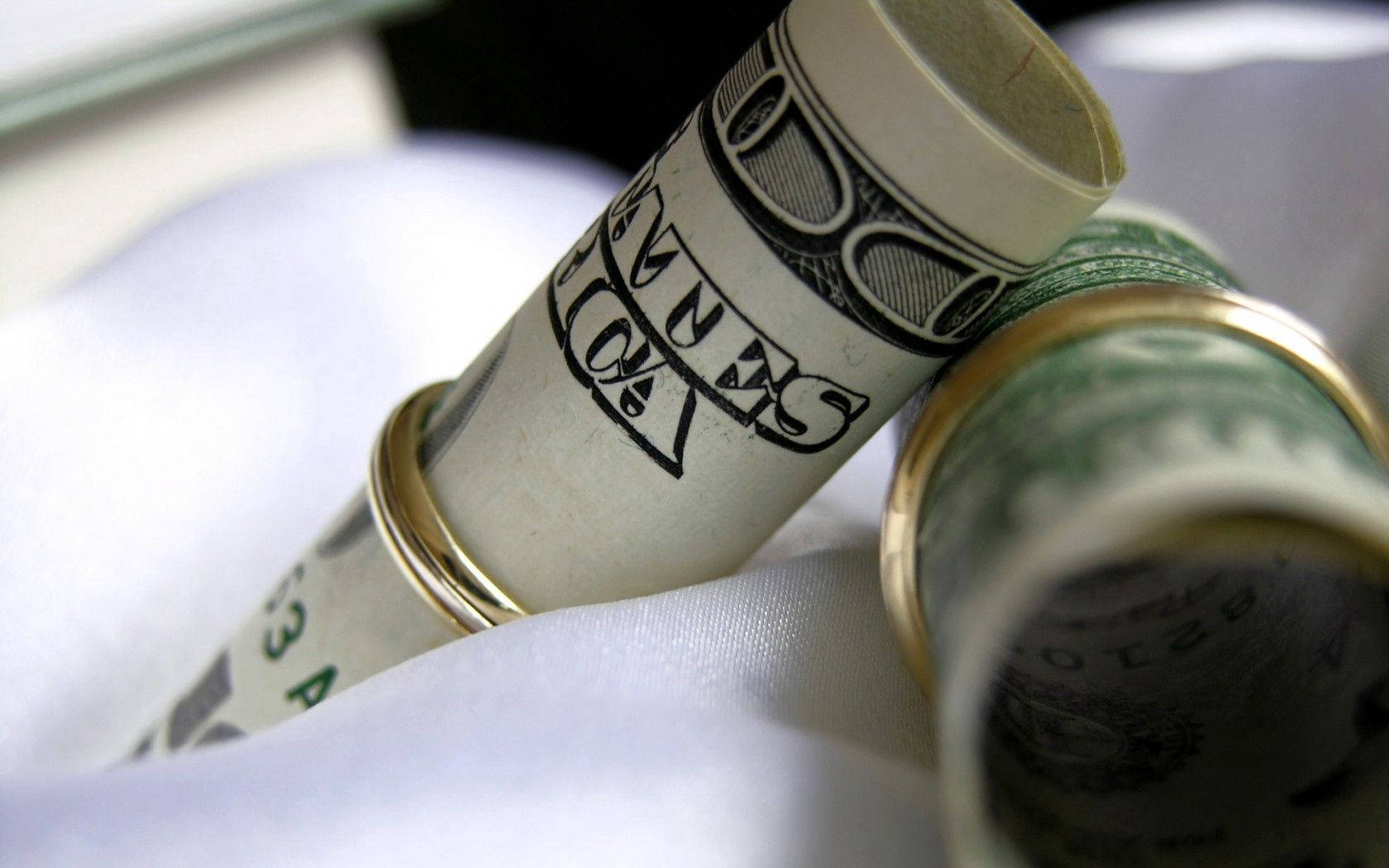 No Money 桌布 壁紙 — 特寫：用金戒指固定的捲起美元紙幣，放在柔軟白色布料上。