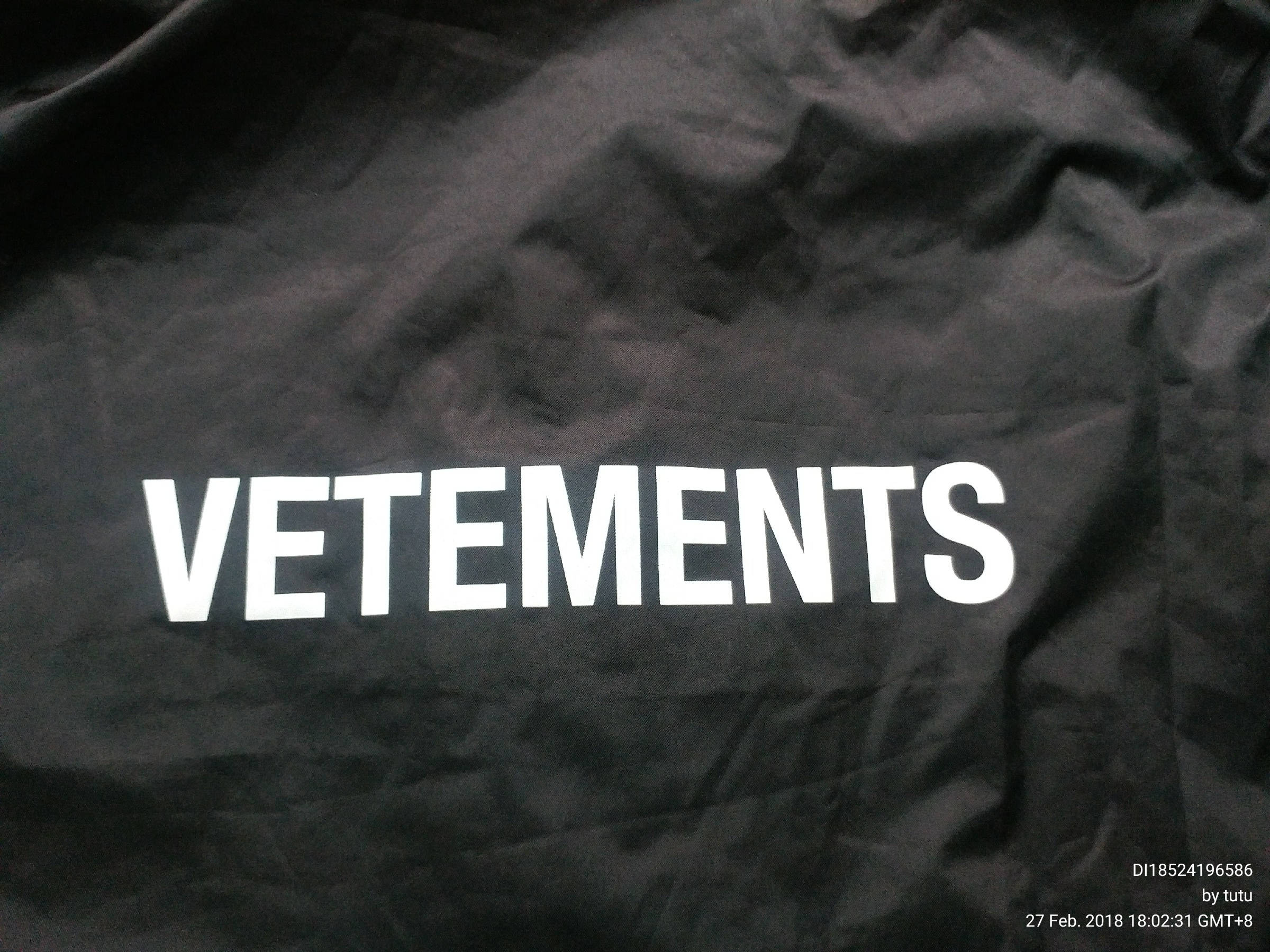 Vetements 桌布 壁紙 — 特寫：皺褶黑色布料上粗體白色VETEMENTS文字，帶有細微紋理和光線對比。