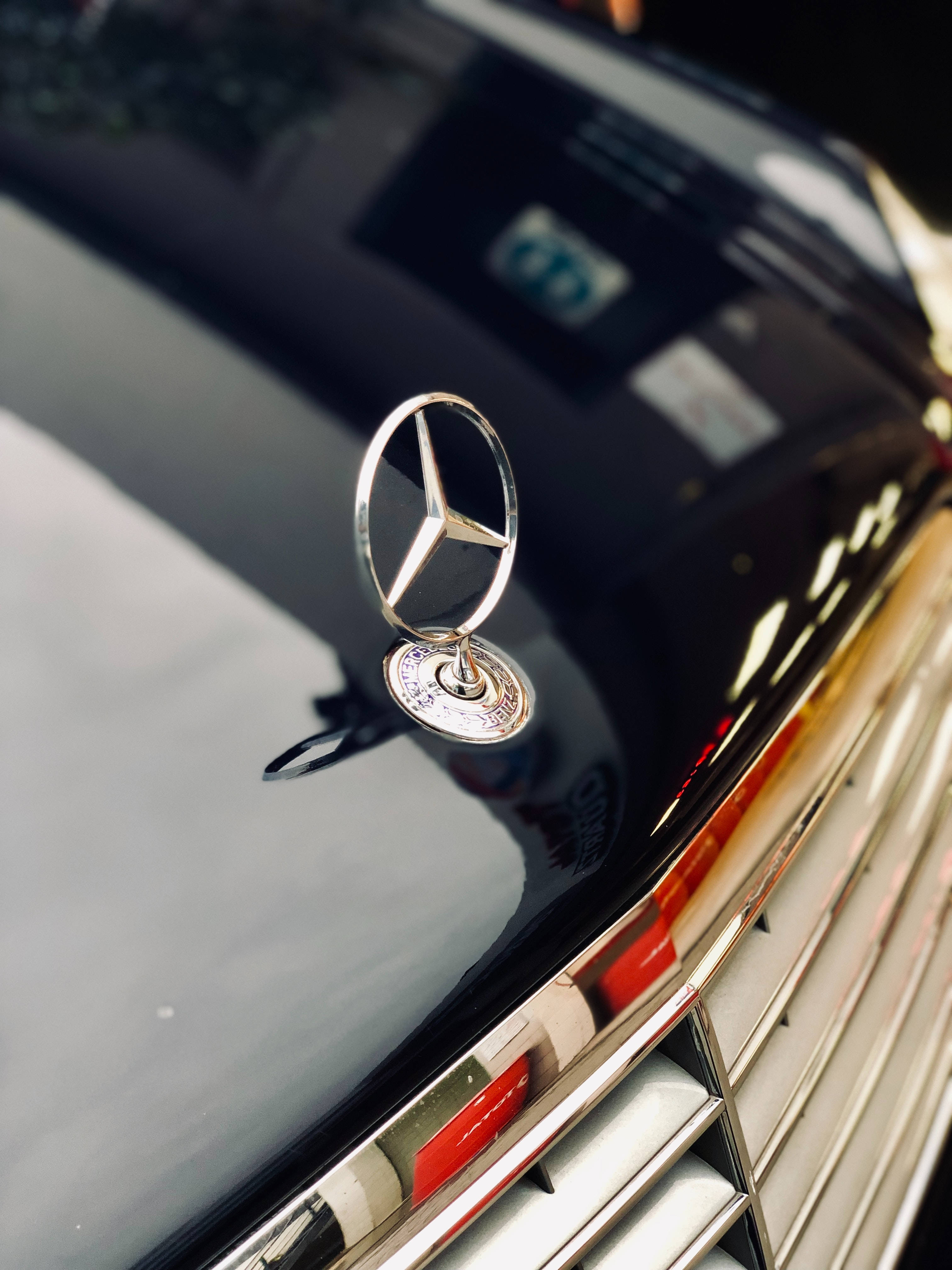 標誌 桌布 壁紙 — 特寫：閃亮銀色 Mercedes-Benz 引擎蓋飾件，置於帶有鍍鉻飾條的亮黑色引擎蓋上。
