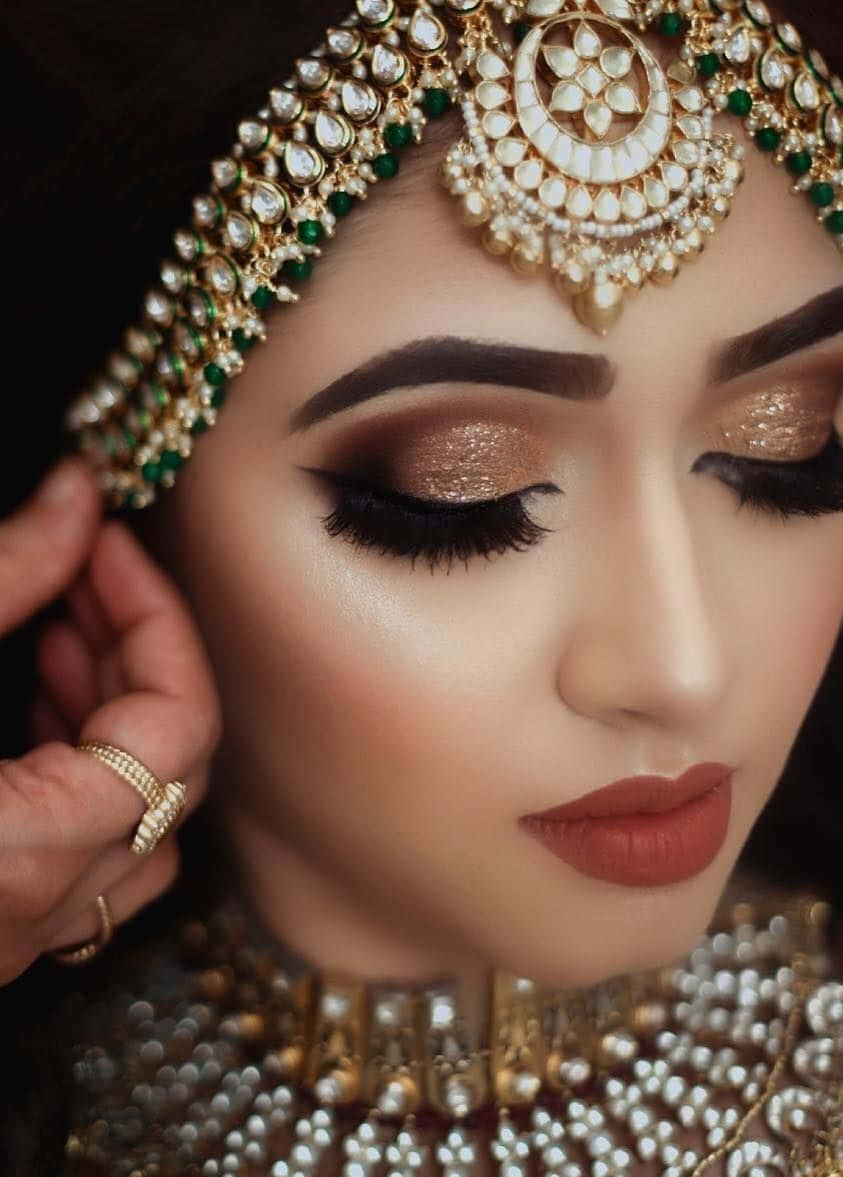 Bride 桌布 壁紙 — 特寫一位女士，佩戴精緻的金色和綠色珠寶，閃爍的化妝，她的手輕輕觸碰太陽穴。