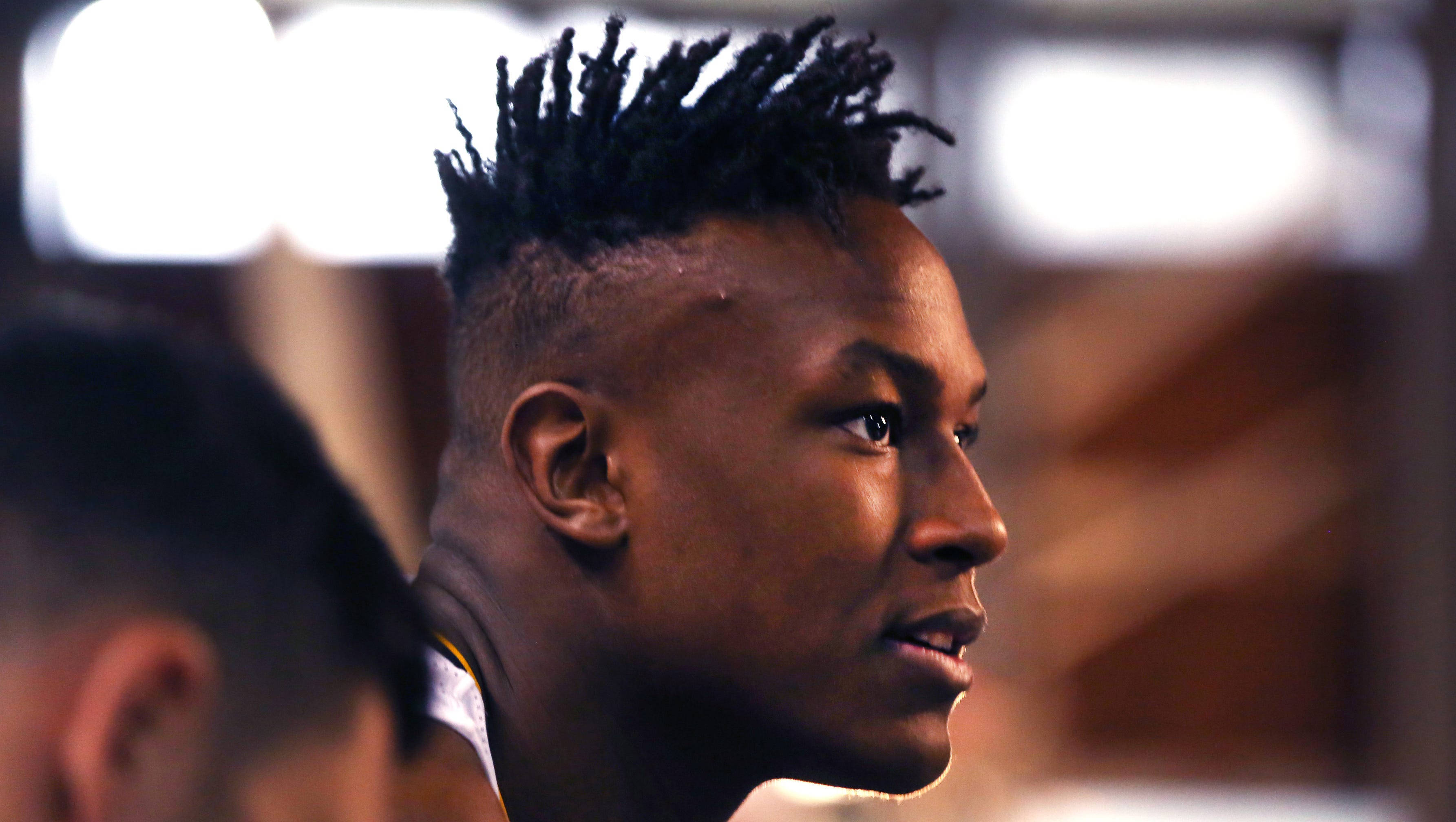 myles turner 桌布 壁紙 — 特寫一位專注的年輕男子，留著尖刺莫霍克髮型，在昏暗的室內環境中專注地向前凝視。