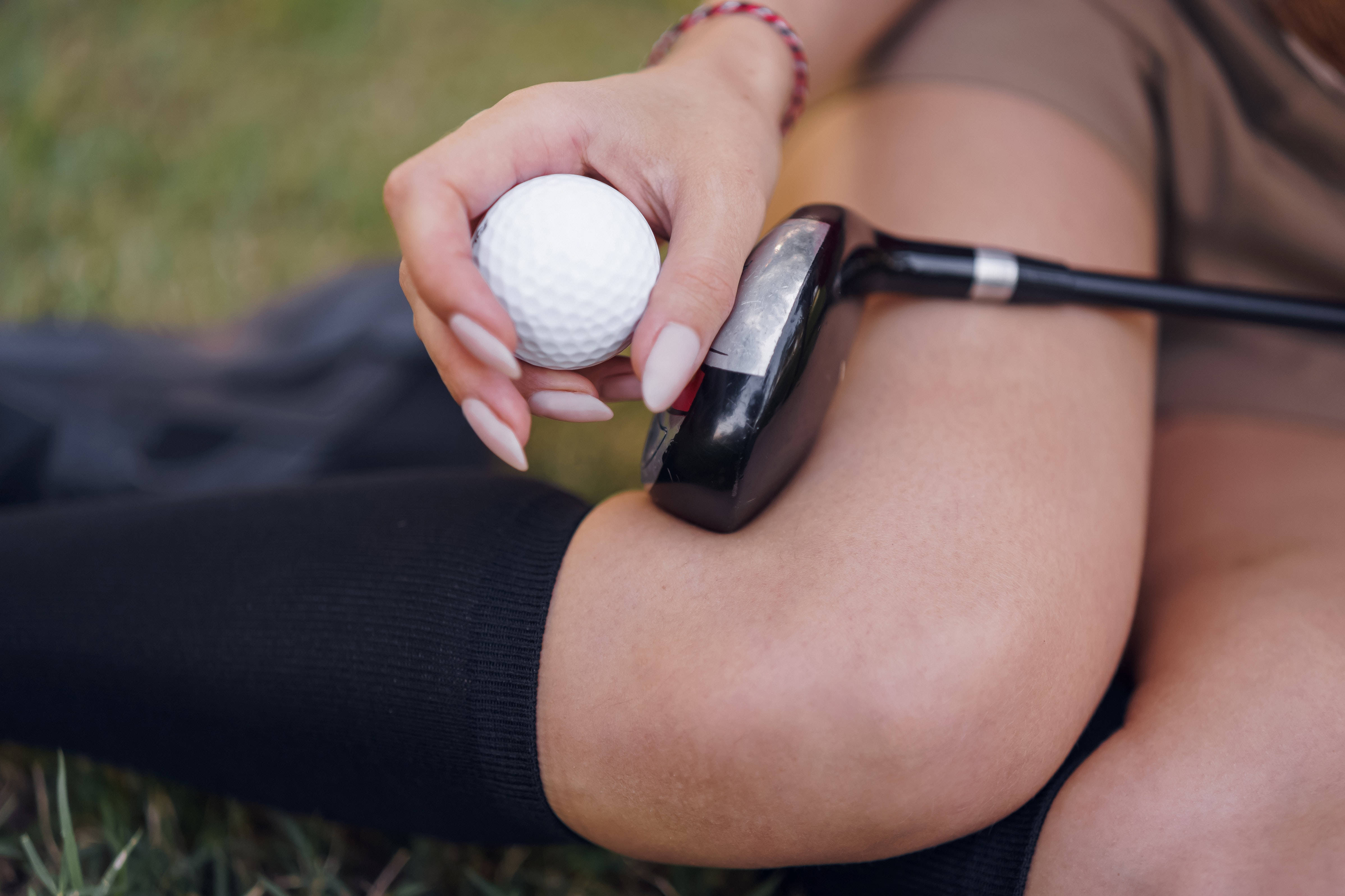 4K Golf 桌布 壁紙 — 特寫一個人的手，在草地上將高爾夫球和球桿放在大腿上。