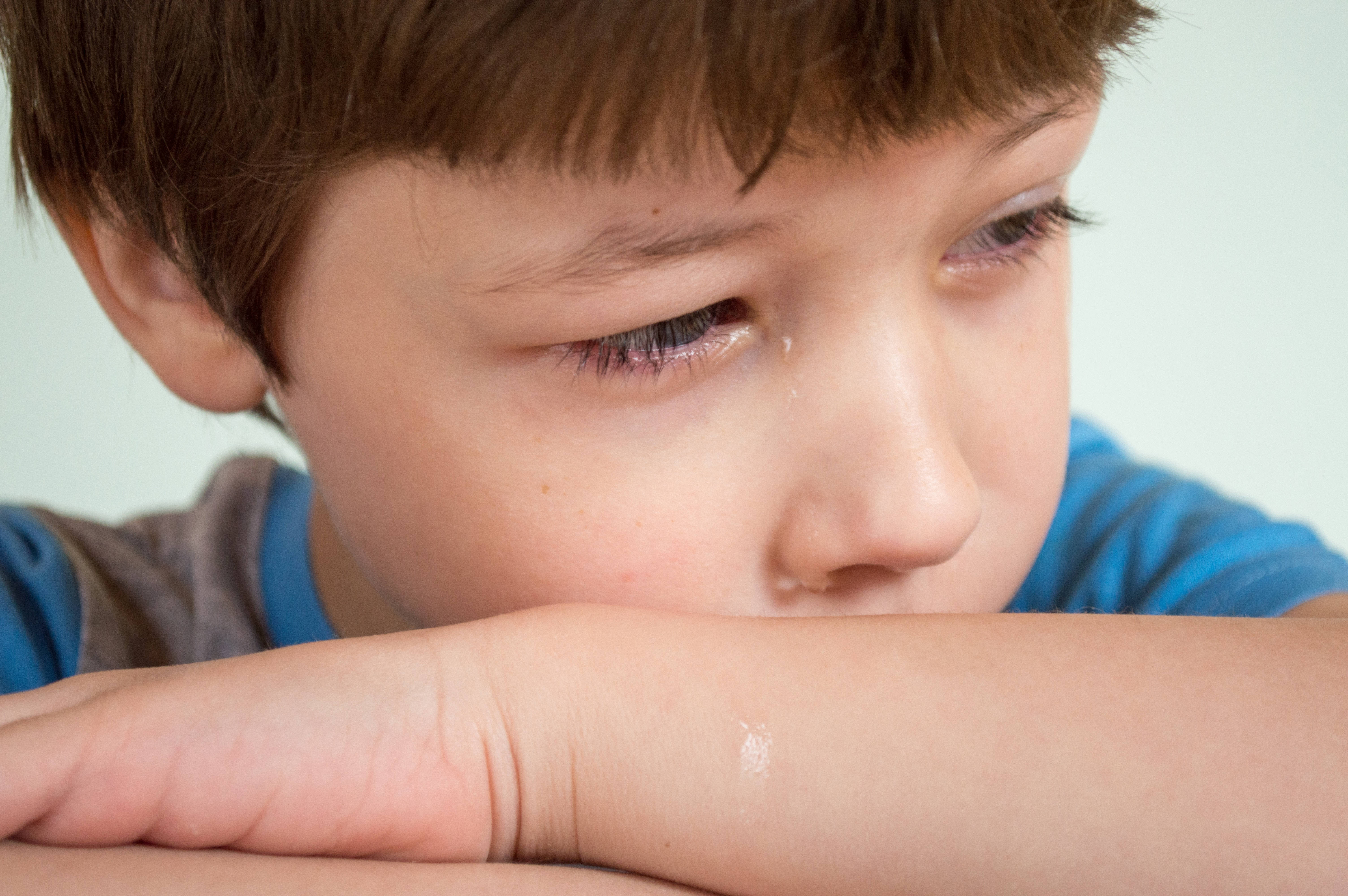 crying sad boy 桌布 壁紙 — 特寫一個年輕男孩淚眼汪汪，將頭靠在手臂上，背景樸素。