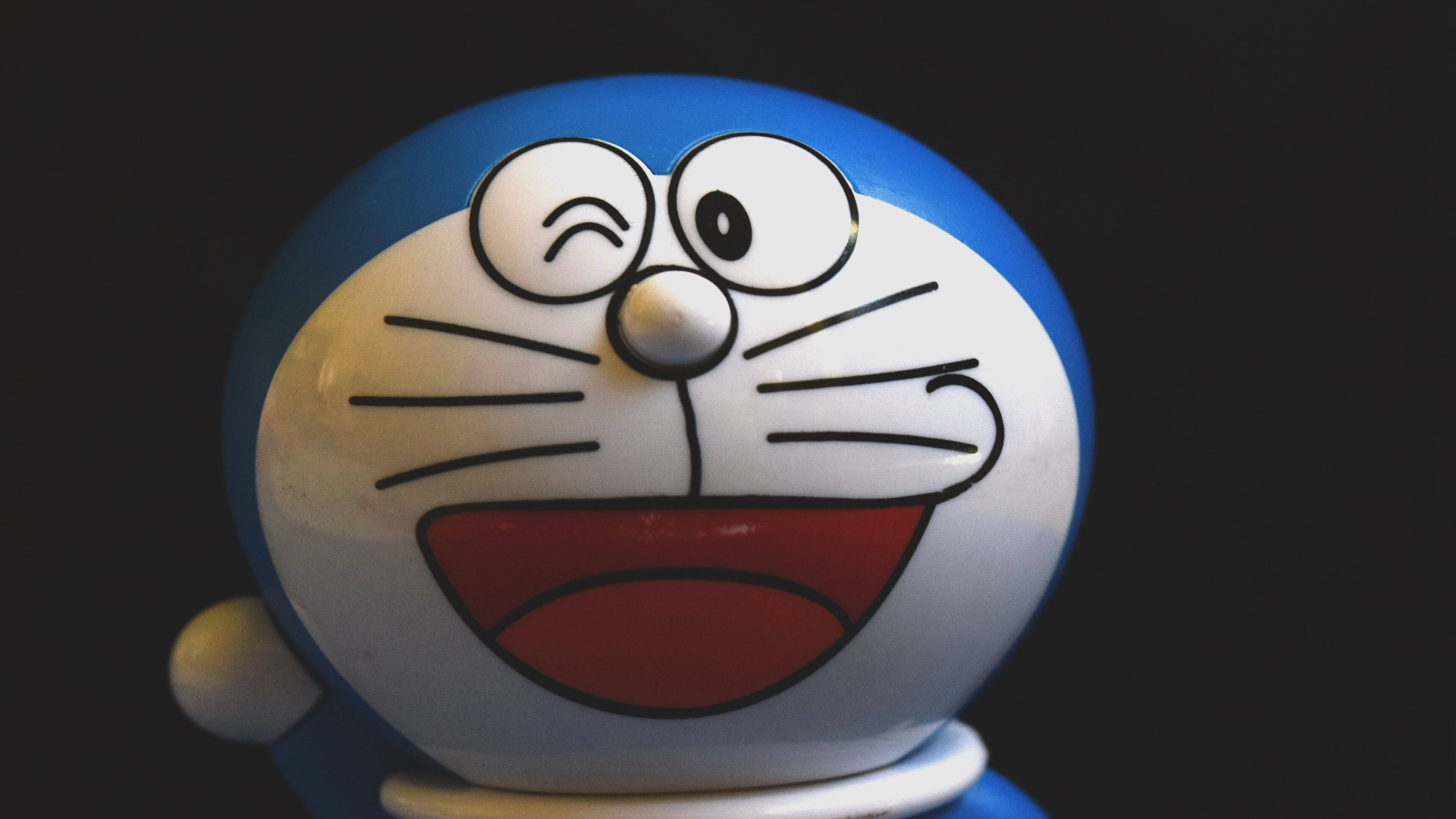 Doraemon 桌布 壁紙 — 特寫一個微笑的藍白色哆啦A夢公仔，在深色背景下單眼眨眼。