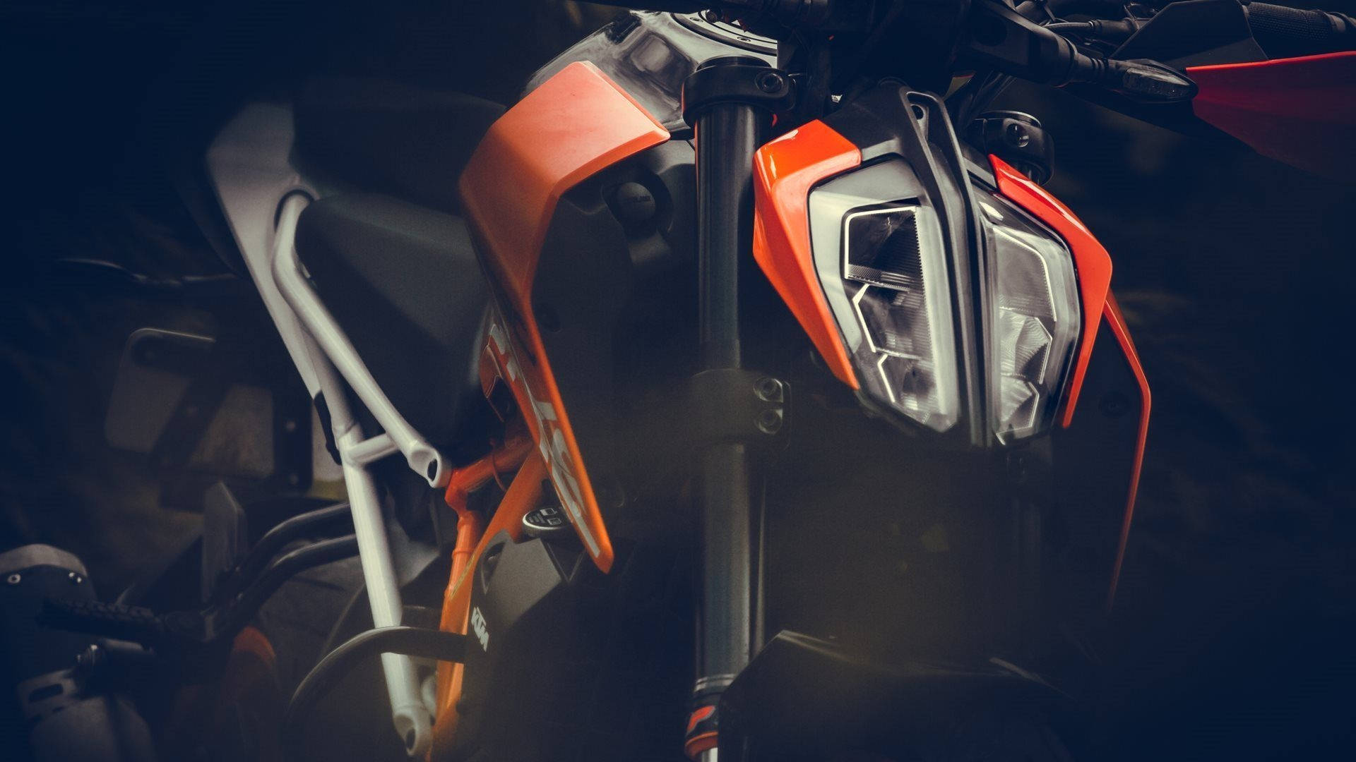 Ktm Bike 桌布 壁紙 — 特寫一個時尚的橙色和黑色機車頭燈，帶有霧面鏡頭和白色框架，背景為深色。
