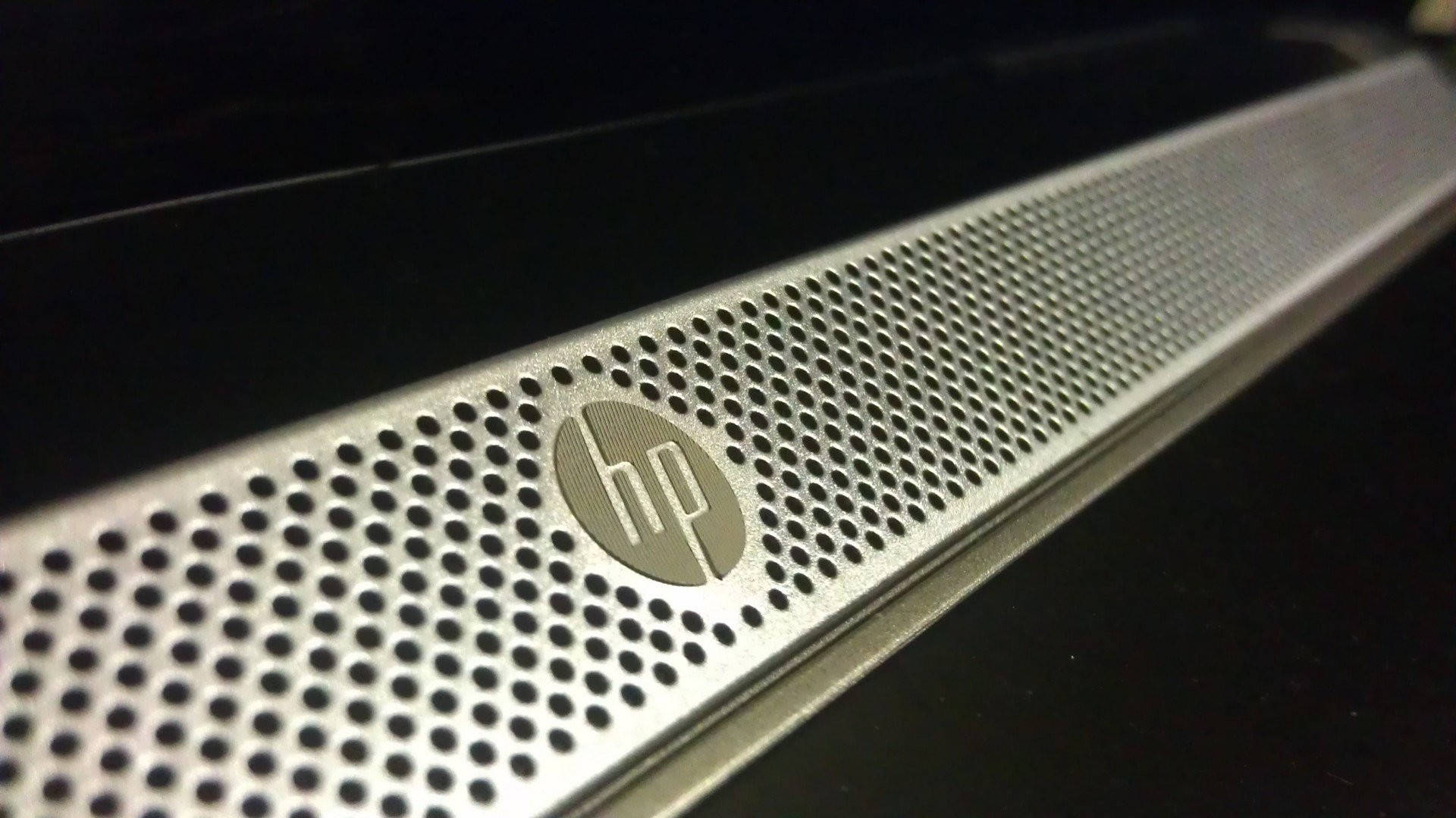 Hp Laptop 桌布 壁紙 — 特寫一個時尚的銀色HP揚聲器格柵，帶有穿孔金屬和標誌，背景為深色。
