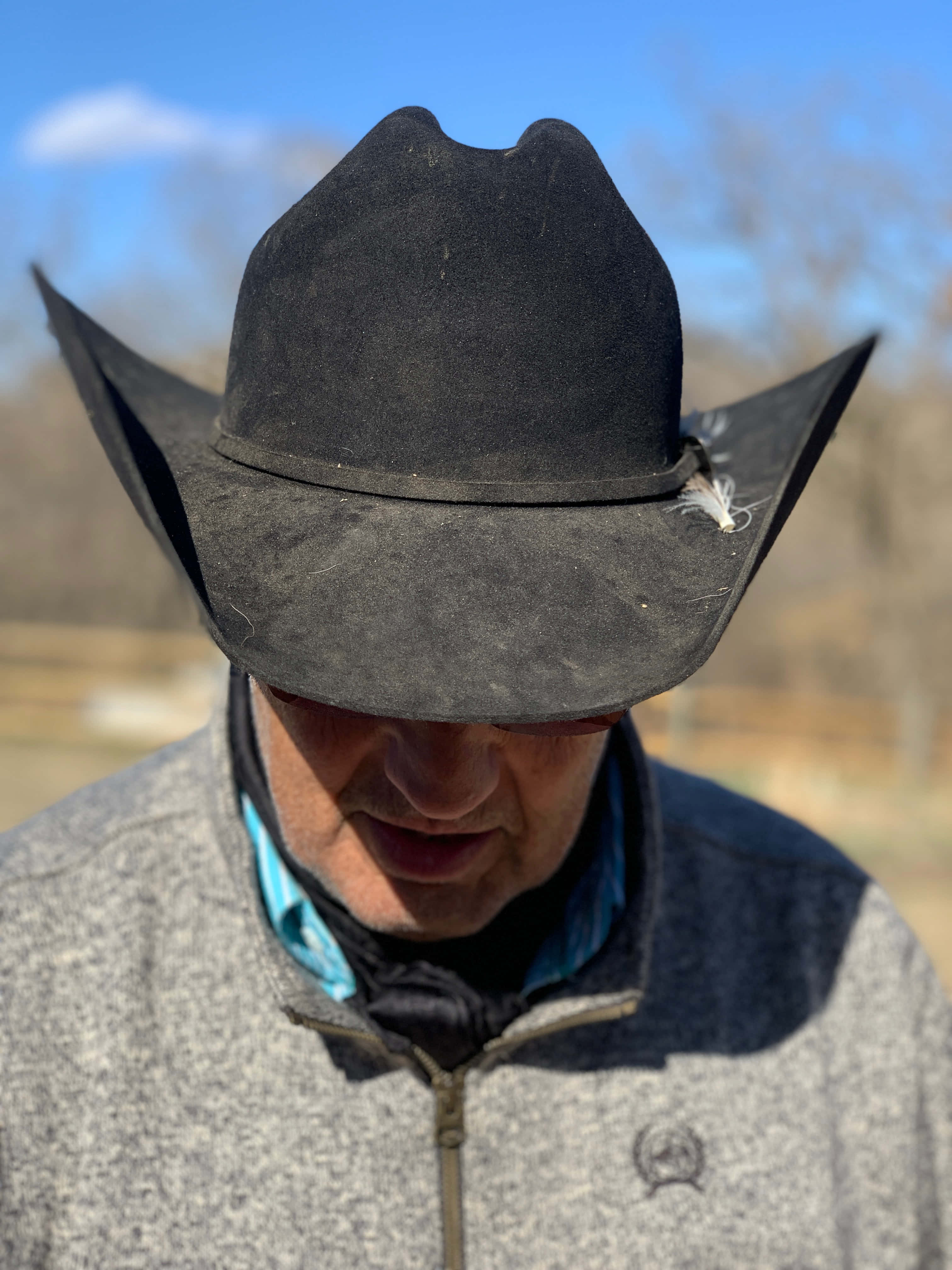 Cowboy Hat 桌布 壁紙 — 特寫一個男人戴著一頂破舊的黑色牛仔帽，帽子上插著一根羽毛，背景是明亮的藍天。