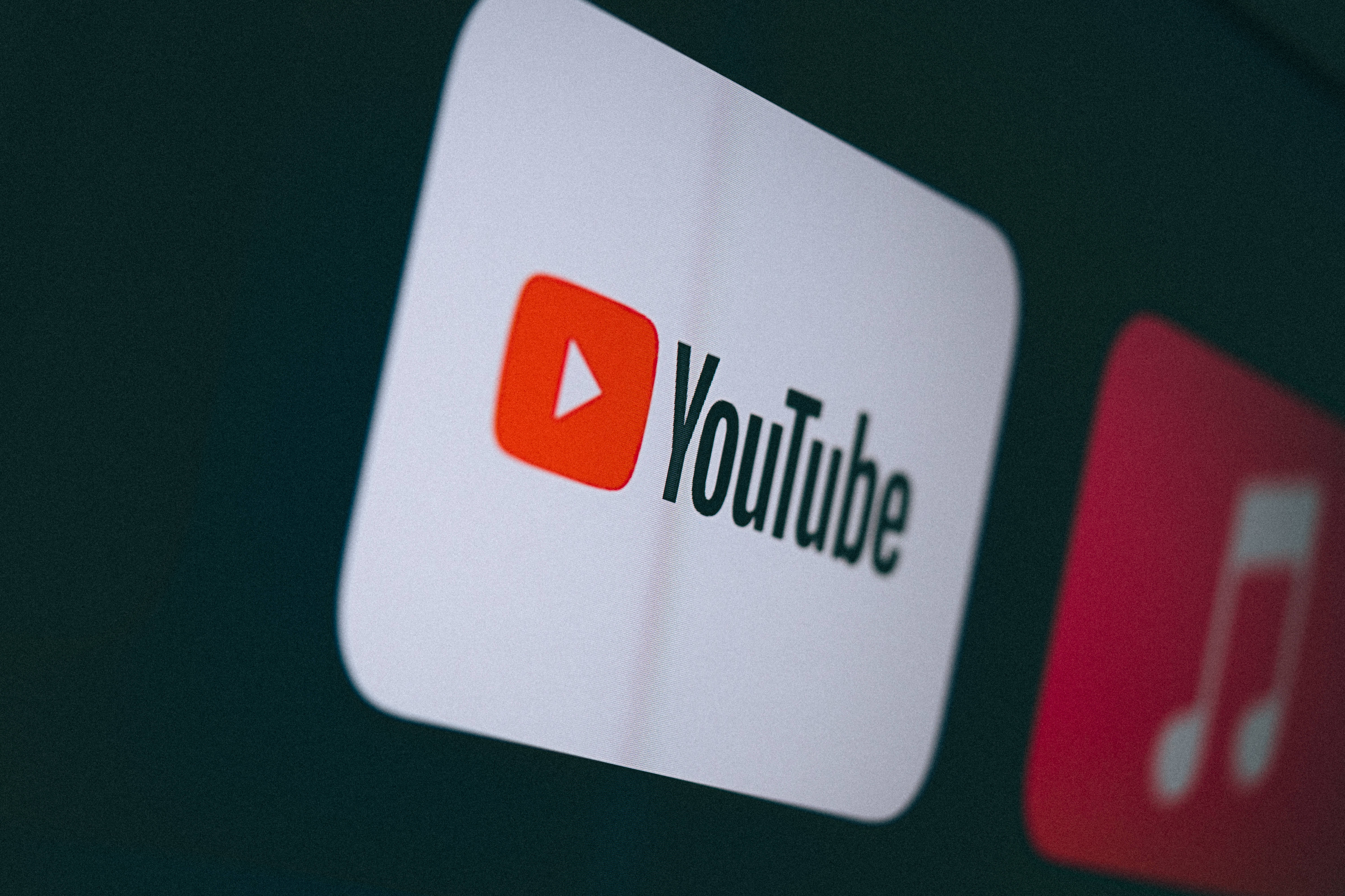 標誌 桌布 壁紙 — 特寫一個發光的 YouTube 應用程式圖示，位於黑暗螢幕上，旁邊有一個模糊的音樂應用程式圖示。