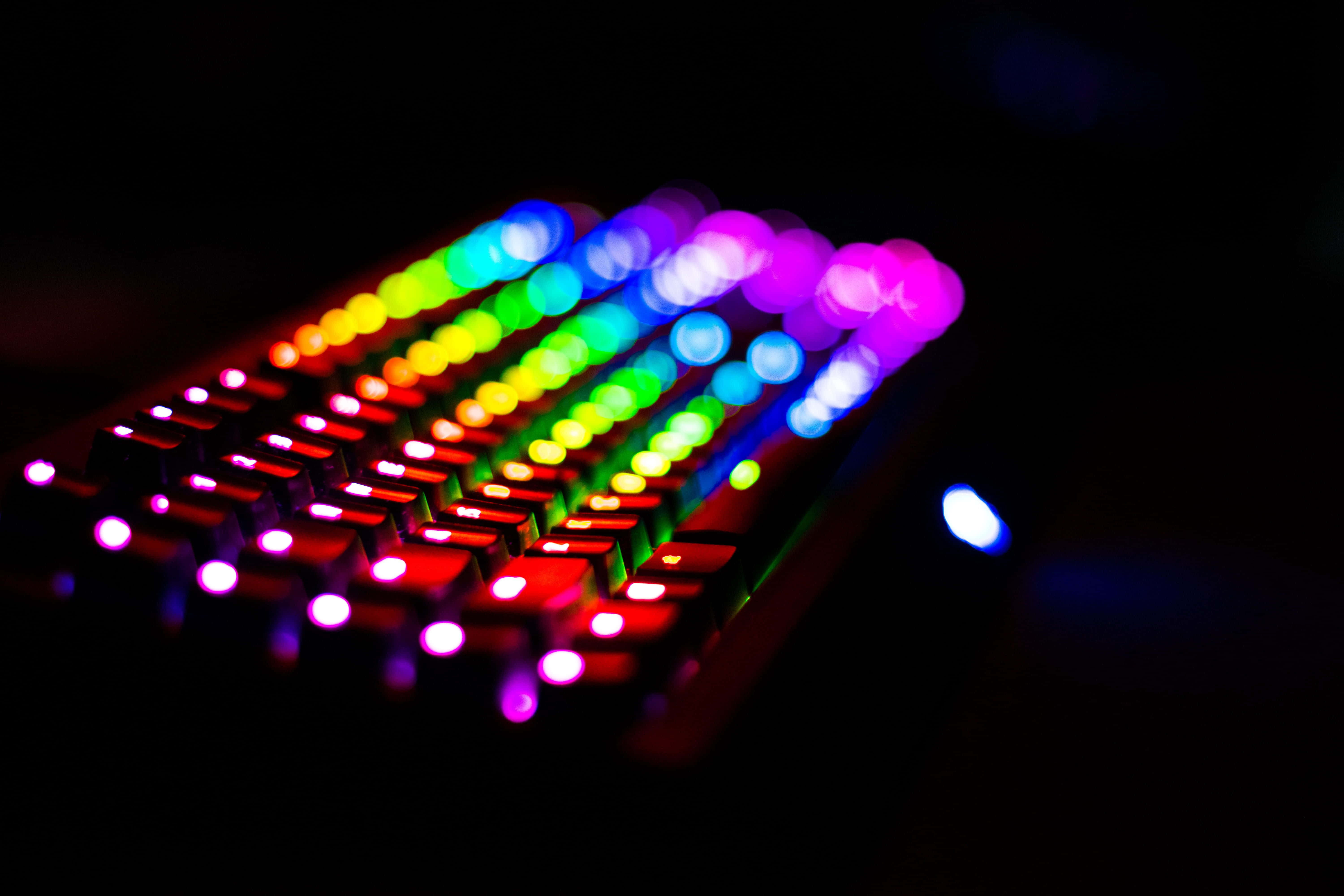 RGB 桌布 壁紙 — 特寫一個發光的彩虹背光鍵盤，在黑暗背景上帶有鮮豔的散景燈光。
