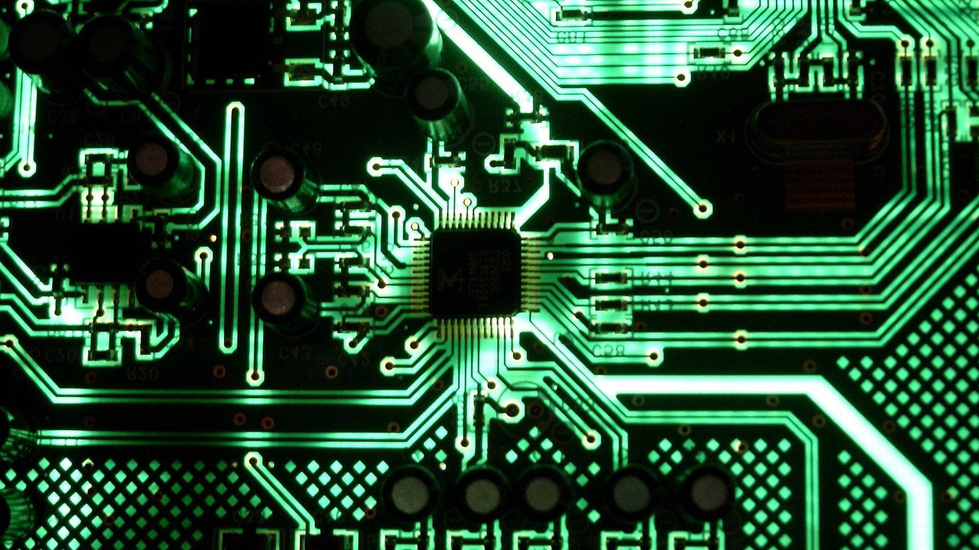 Circuit 桌布 壁紙 — 特寫一個發光的綠色電路板，帶有複雜的路徑和一個中央晶片，在黑暗背景下被照亮。