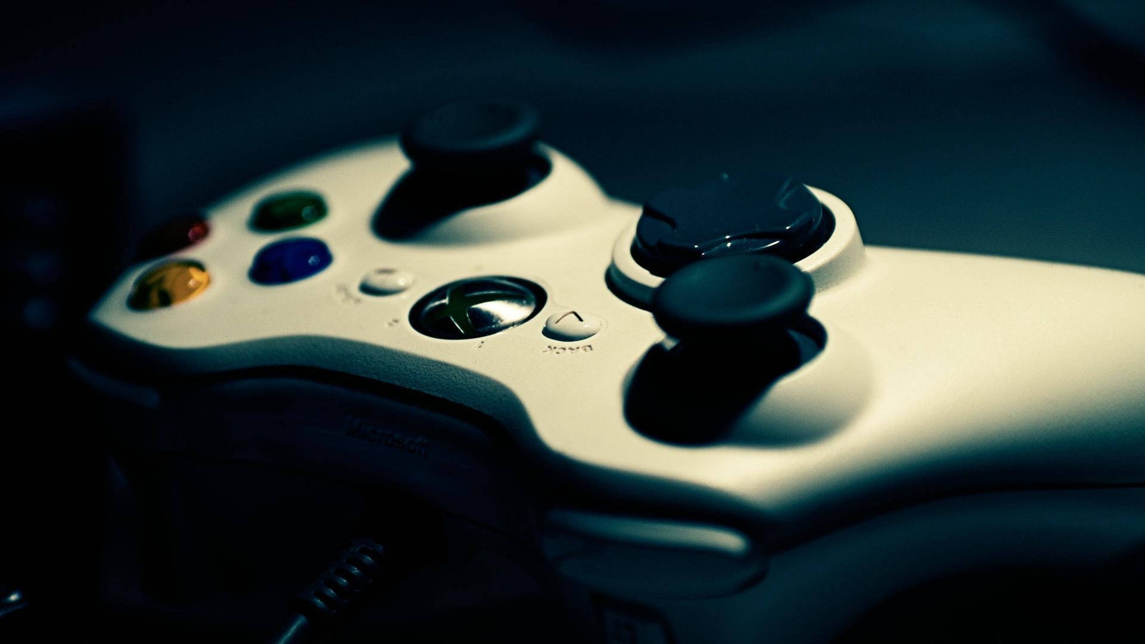 Xbox 桌布 壁紙 — 特寫一個白色 Xbox 360 控制器，帶有彩色按鈕和黑色搖桿，在憂鬱的藍色燈光下。