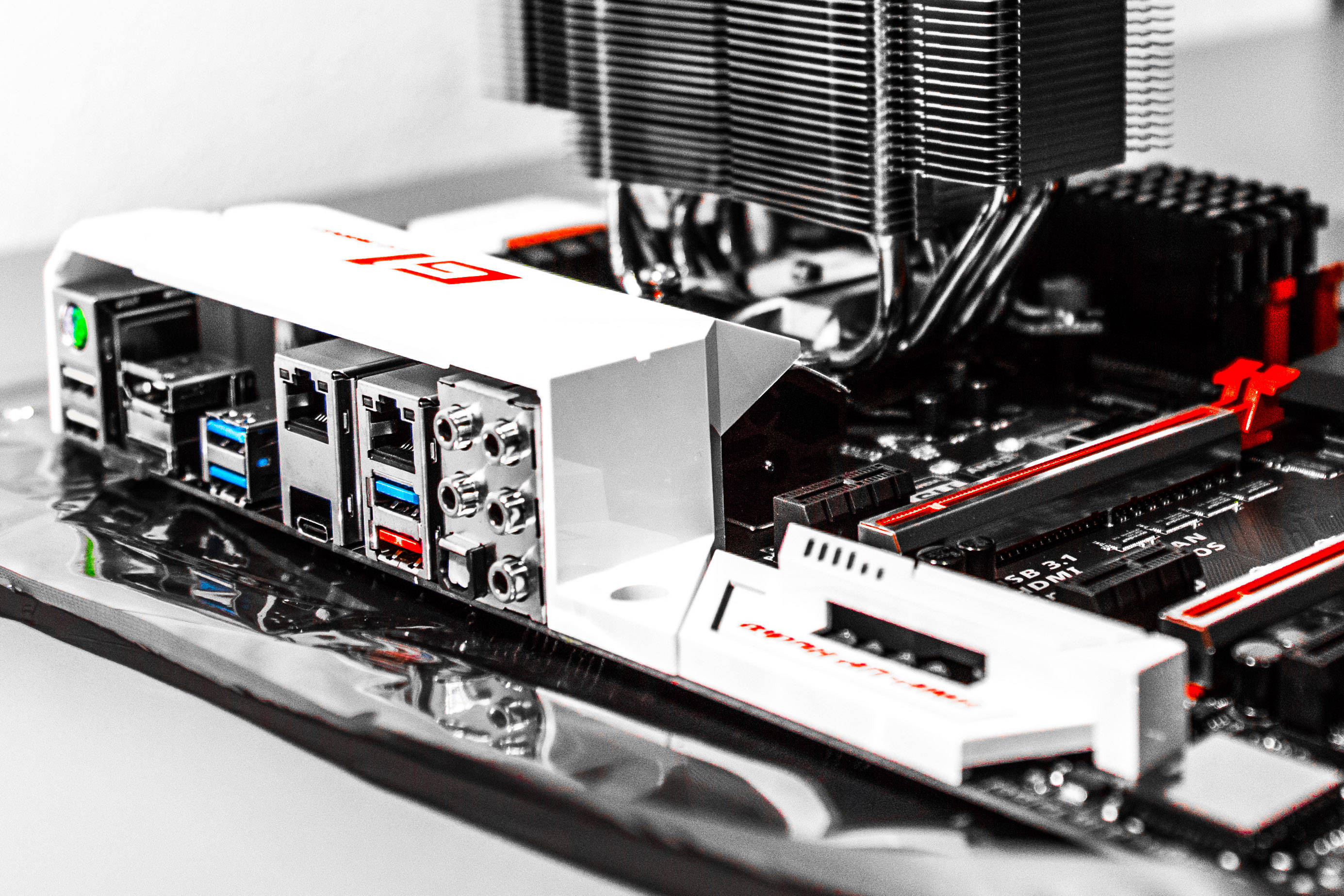 Motherboard 桌布 壁紙 — 特寫一個白色和黑色的遊戲主機板，帶有紅色點綴和可見的端口，放置在反光表面上。