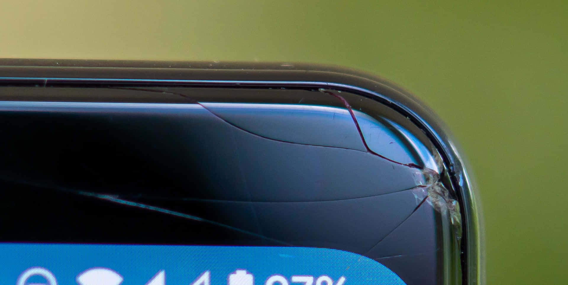 裂屏 桌布 壁紙 — 特寫一個破裂的智慧型手機螢幕，顯示靠近右上角的損壞，背景為綠色。