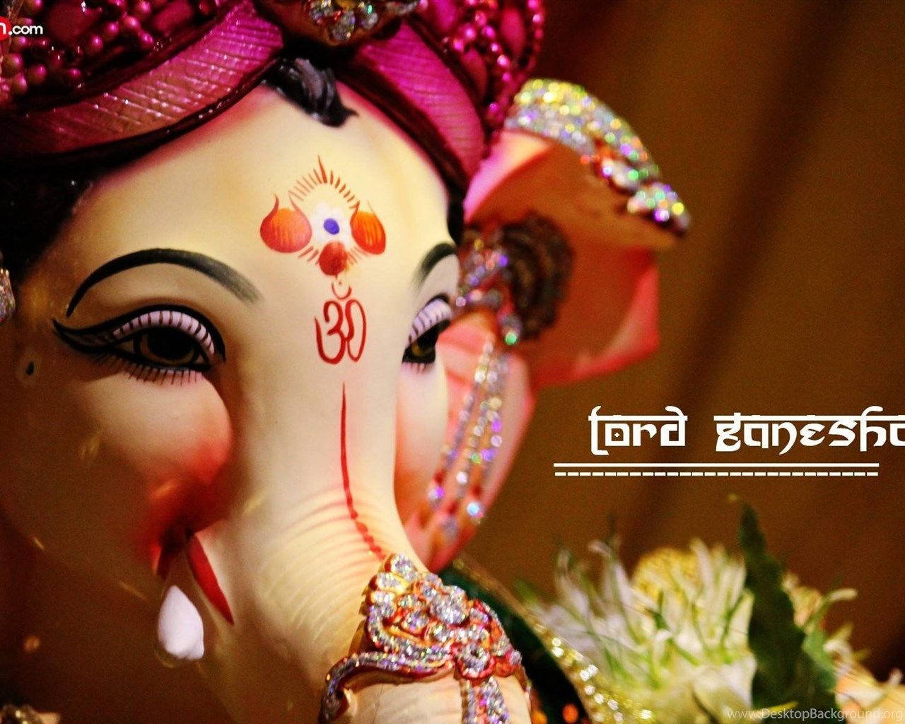 Ganesh 桌布 壁紙 — 特寫一個裝飾華麗的象神像，戴著鑲有寶石的皇冠和紅色蒂拉克，背景是溫暖的金色。