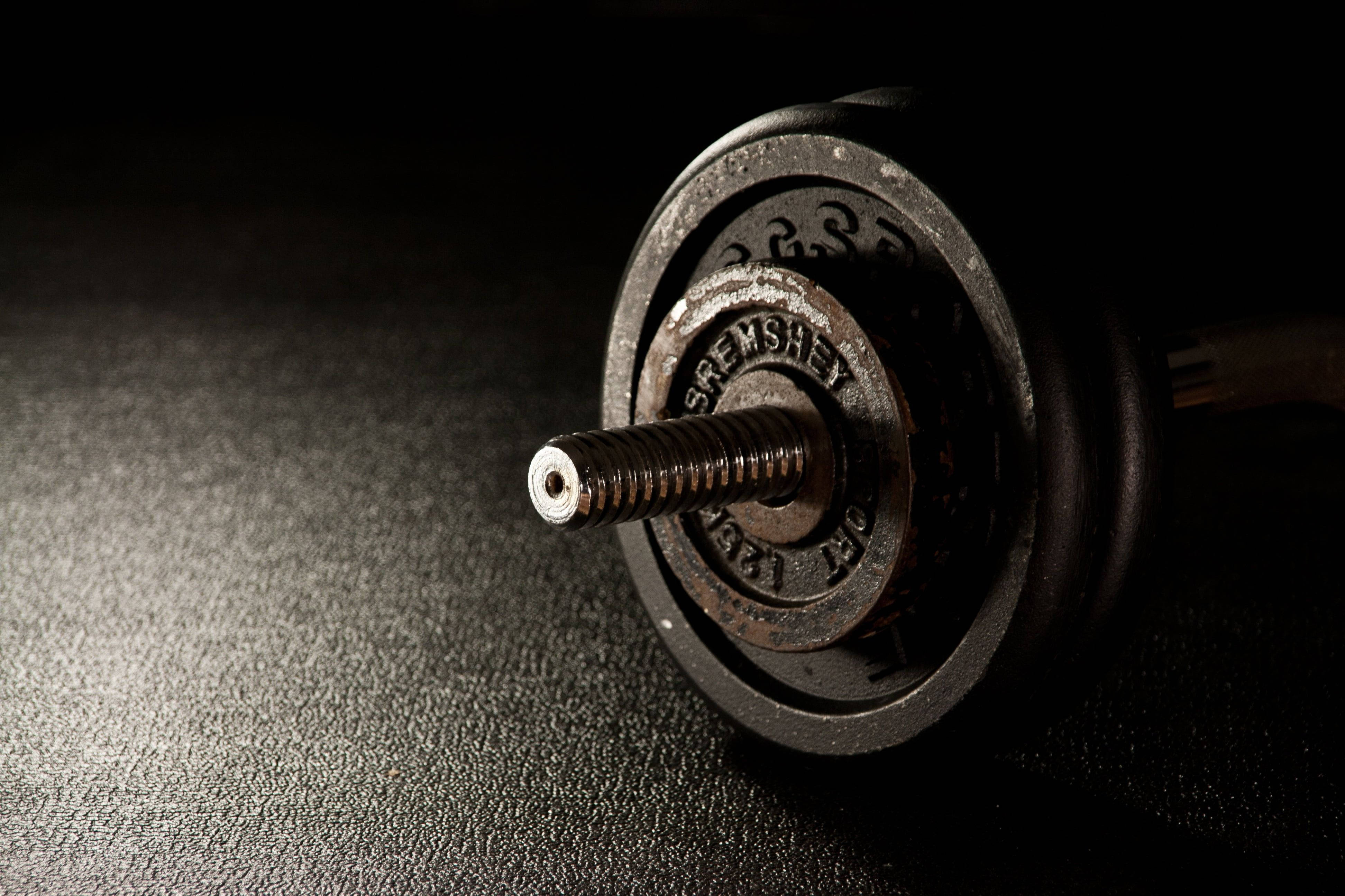 Barbell 桌布 壁紙 — 特寫一個重型槓鈴配重片，上面有明顯磨損和刻字，背景是深色紋理表面。