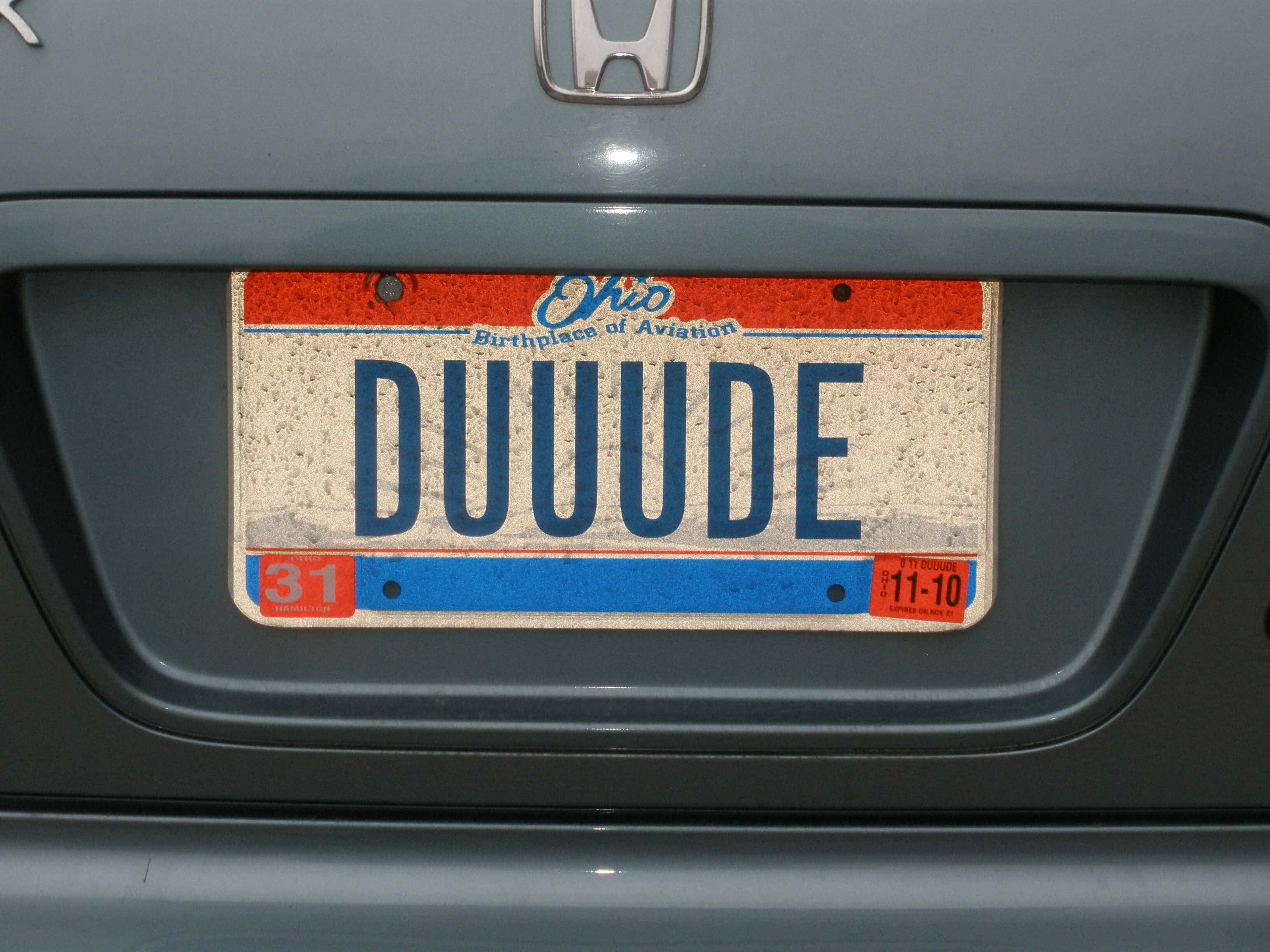 License Plate 桌布 壁紙 — 特寫一個風化的俄亥俄州車牌，上面寫著 DUUUDE，安裝在灰色本田汽車的保險桿上。