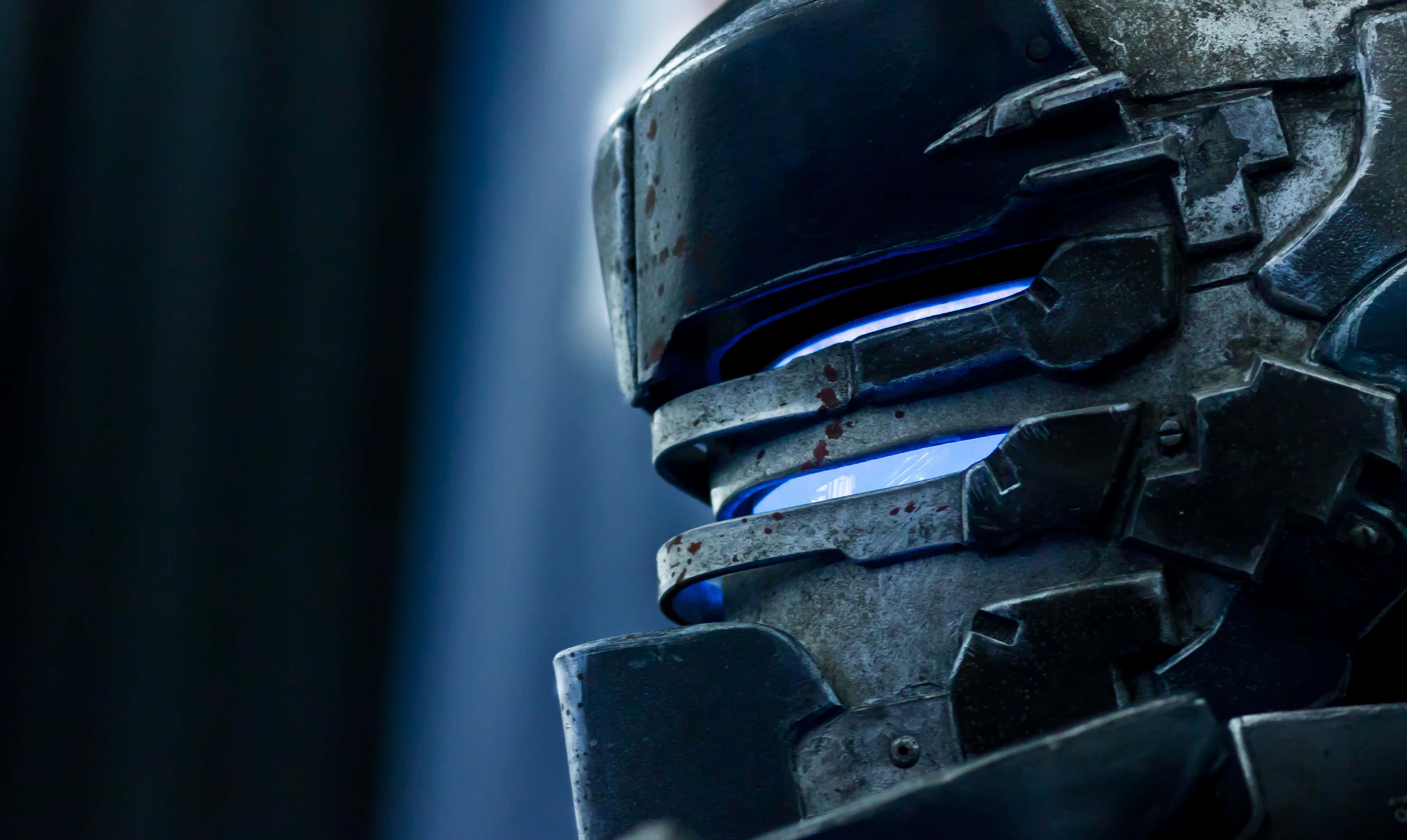 Dead Space 4K 桌布 壁紙 — 特寫一個風化的未來主義頭盔，帶有發光的藍色眼睛和血跡，背景是深藍色模糊的。