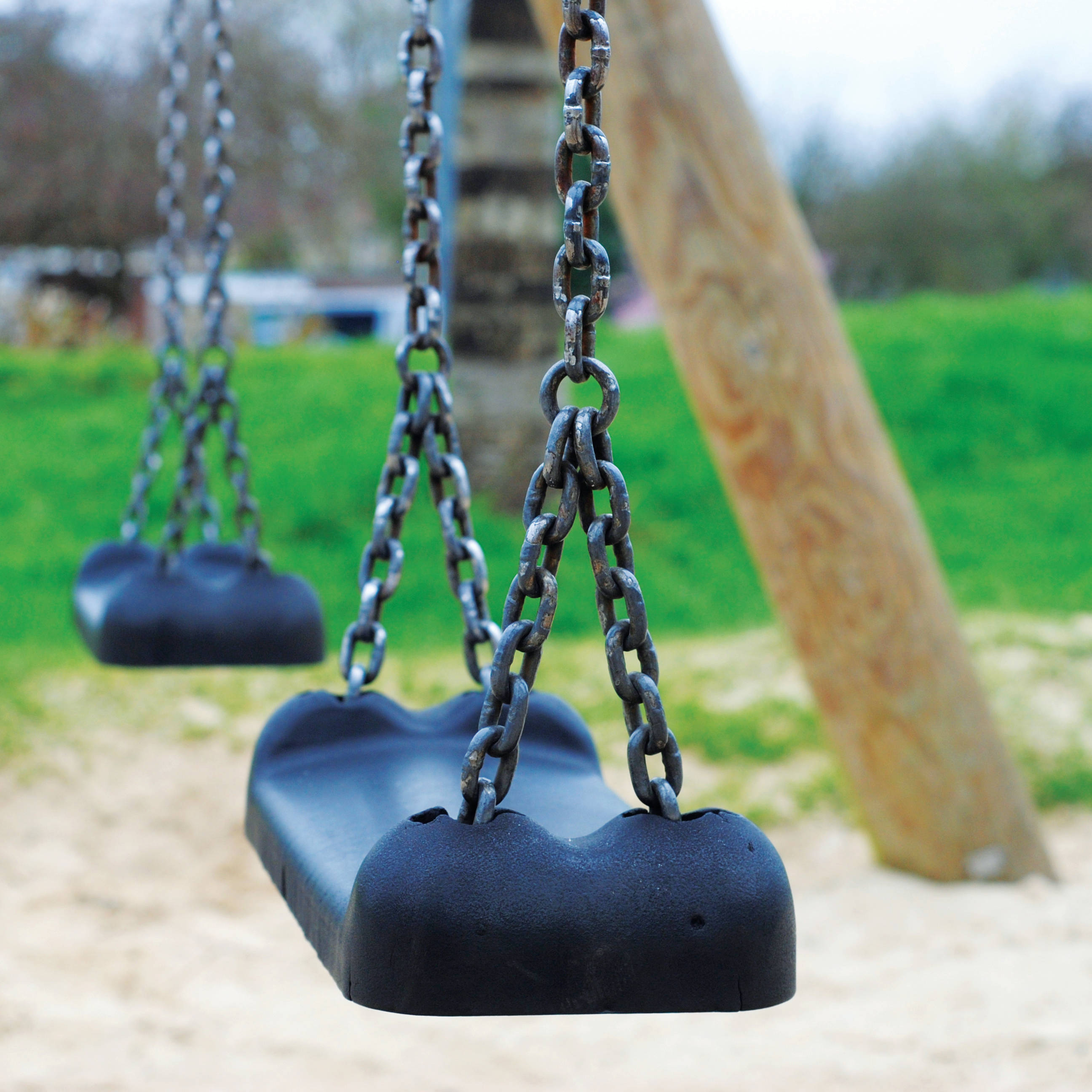 Playground 桌布 壁紙 — 特寫一個黑色塑料鞦韆，用生鏽的鏈條懸掛在草地遊樂場的木柱上。