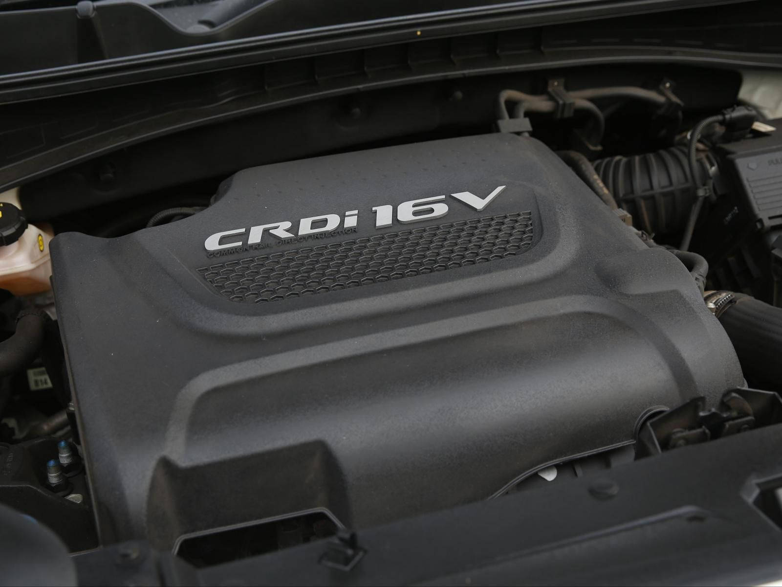 Kia 桌布 壁紙 — 特寫一個黑色引擎蓋，上面標有 CRDi 16V，位於汽車打開的引擎蓋內，周圍有機械部件。