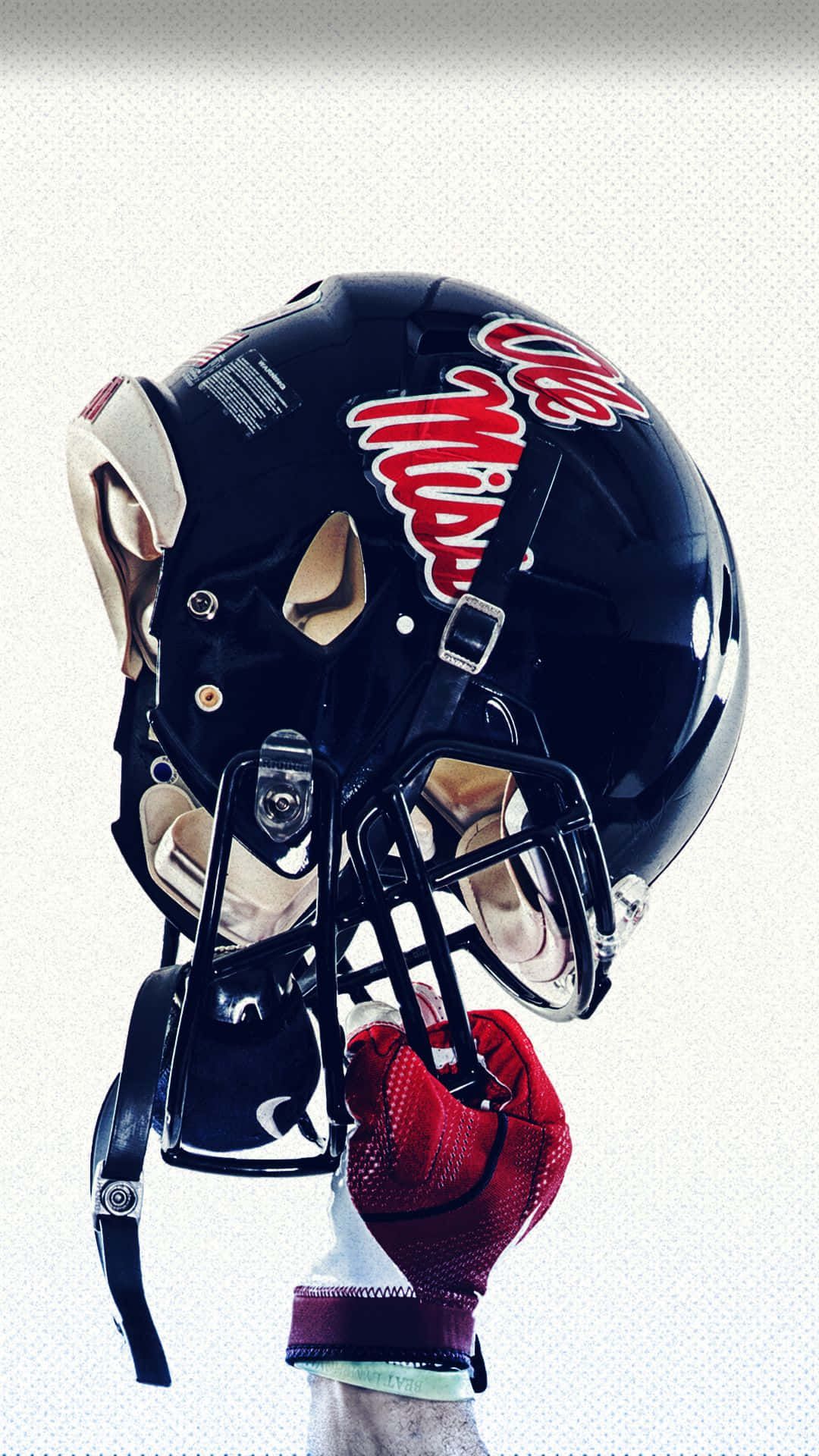 運動 桌布 壁紙 — 特寫一個黑色美式足球頭盔，帶有紅色'Ole Miss'字樣，由戴紅色手套的手拿著，背景為有紋理的白色。