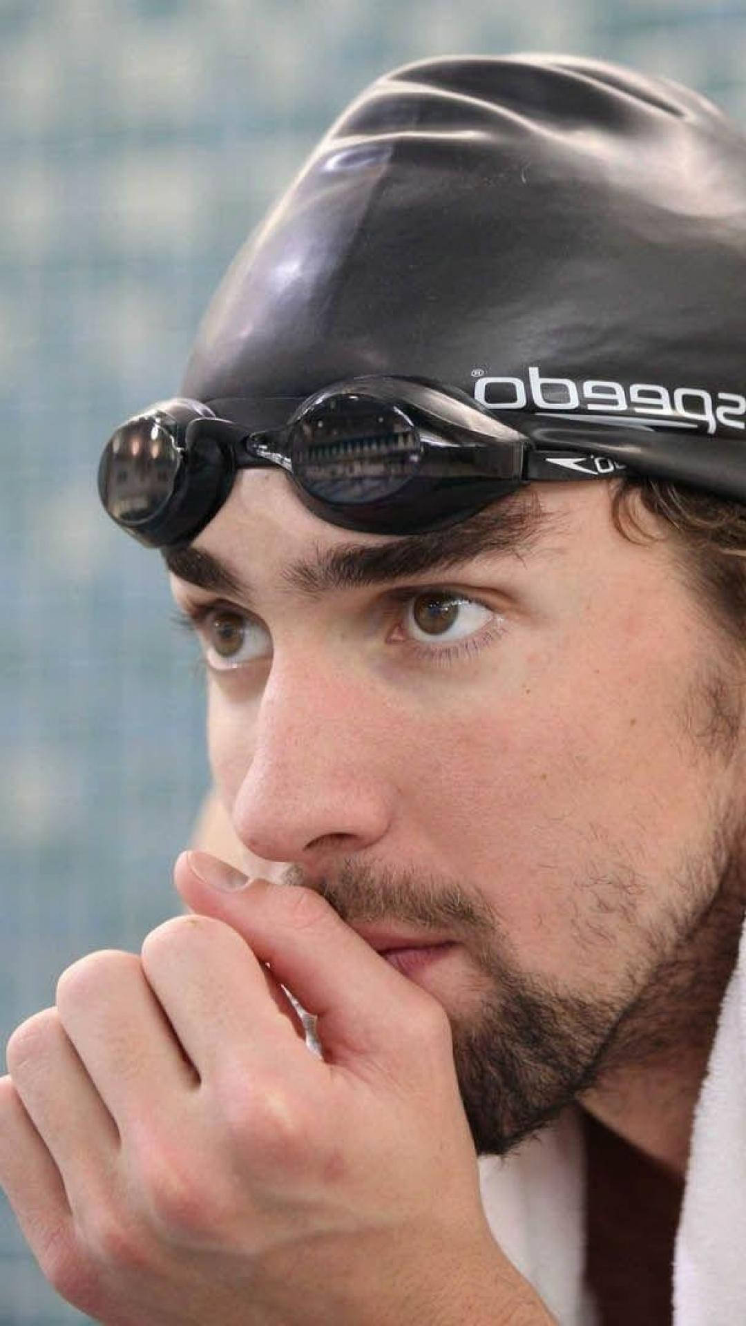michael 桌布 壁紙 — 特寫一名專注的男性泳手，戴黑色泳帽和泳鏡，泳鏡擱在額頭上，手靠近嘴巴。
