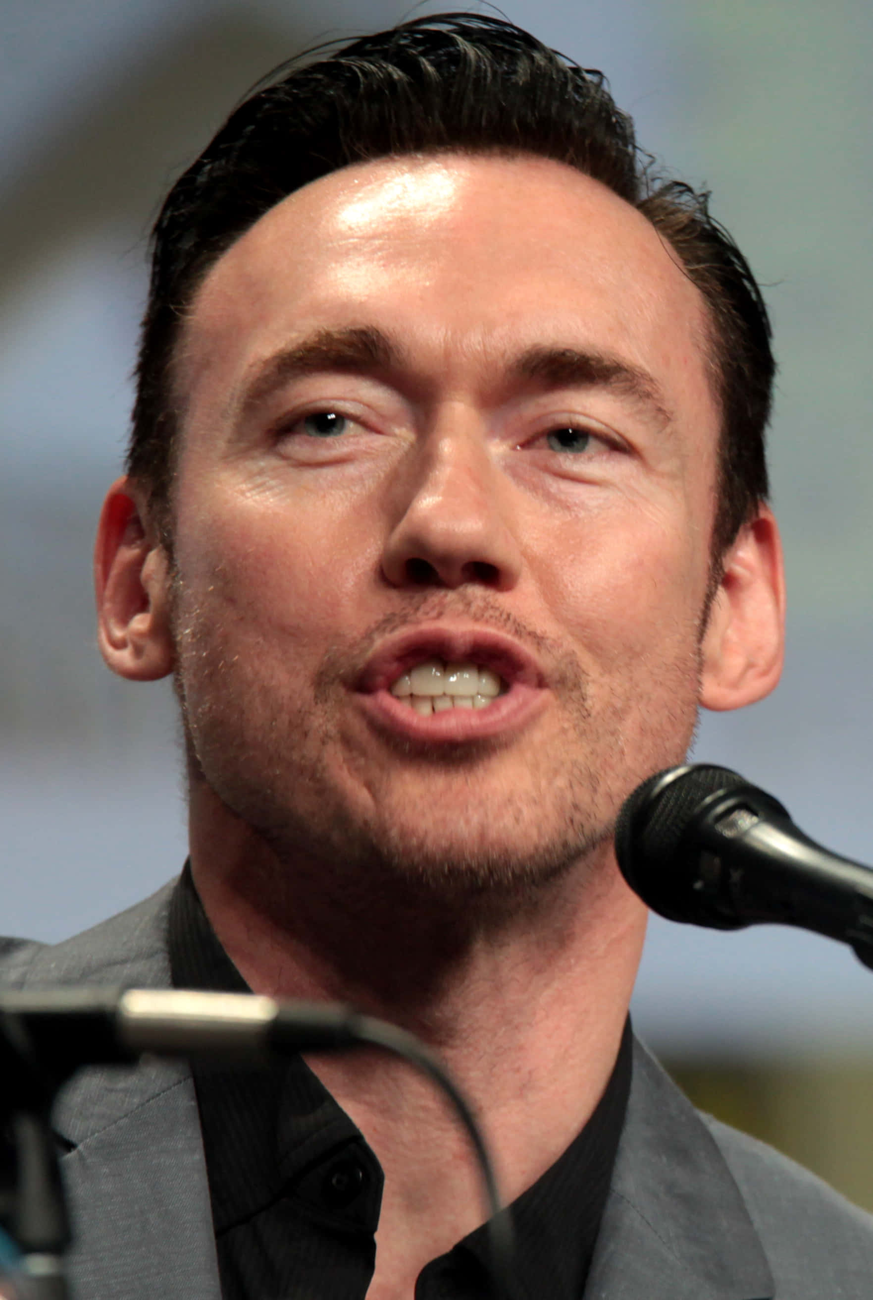 Kevin Durand 桌布 壁紙 — 特寫一名深色頭髮、鬍渣的男人在座談會上對著麥克風發言。