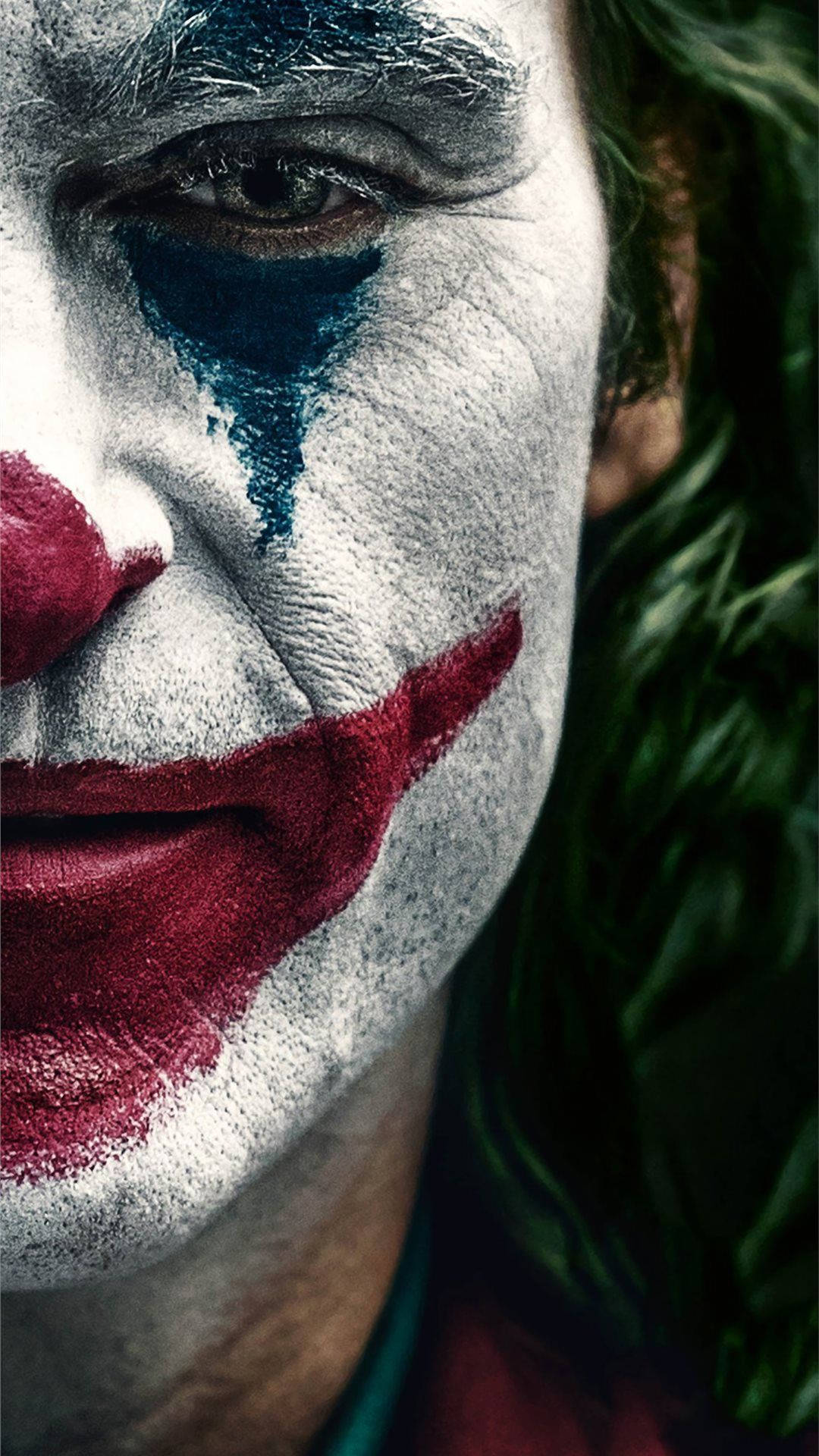 Joker 2019 桌布 壁紙 — 特寫一名男子，臉上塗有白色顏料、紅唇和藍色淚痕，傳達強烈情感。