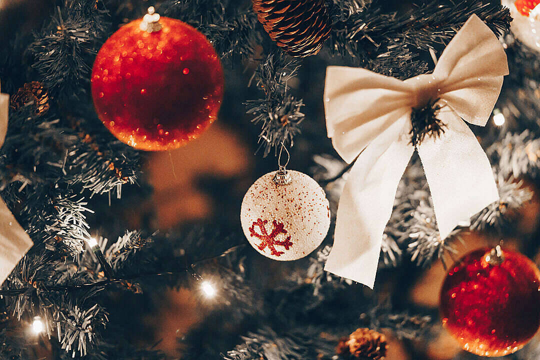 Red Christmas 桌布 壁紙 — 特寫一棵溫暖照明的聖誕樹，裝飾著紅色閃亮飾品、松果和奶油色蝴蝶結。