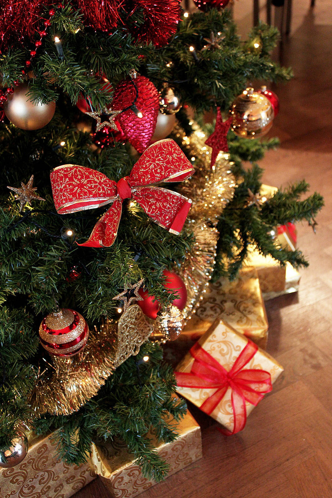 美麗聖誕 桌布 壁紙 — 特寫一棵茂盛的綠色聖誕樹，裝飾著紅色蝴蝶結、金色亮片和閃亮飾品，樹底有包裝好的禮物。