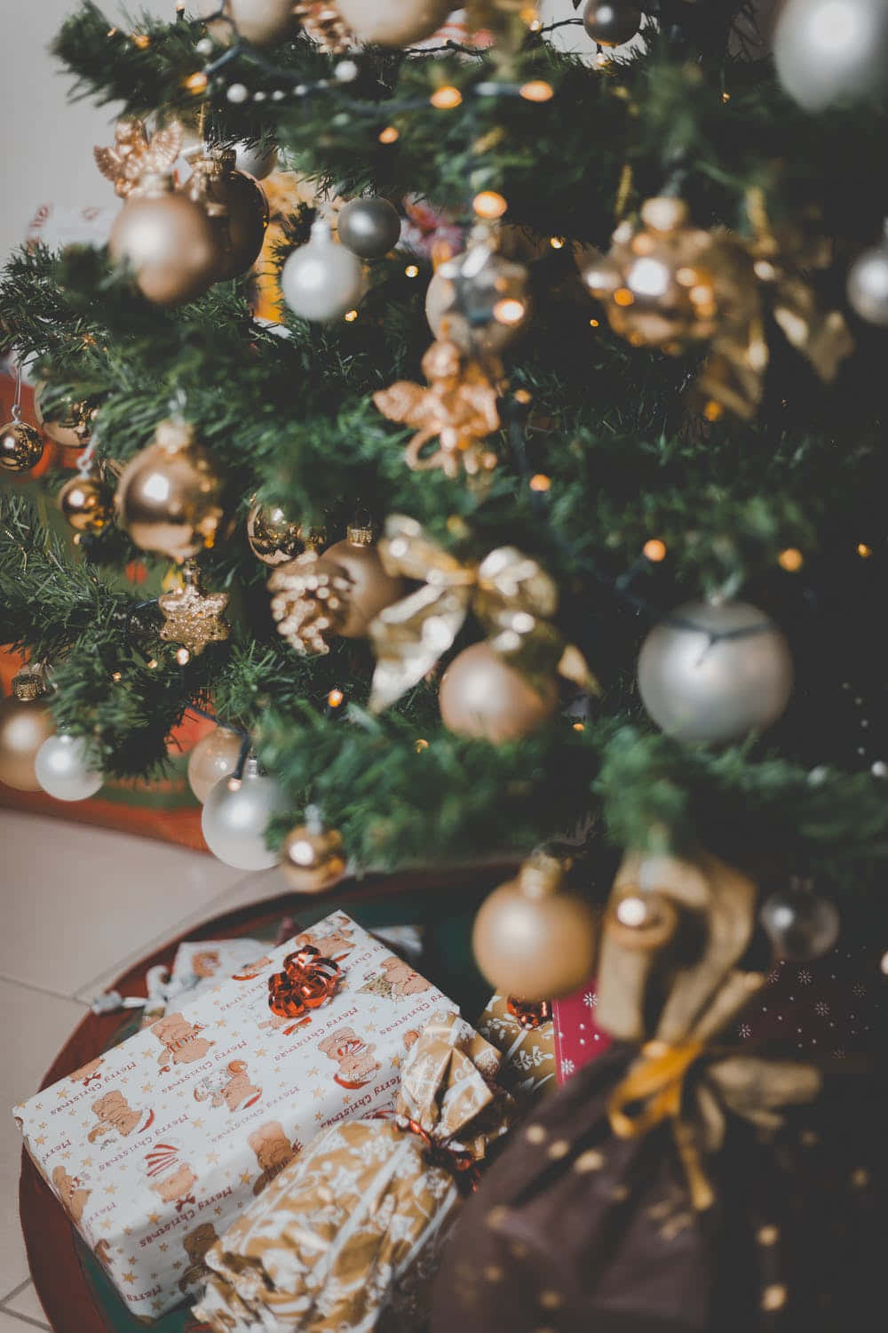 Aesthetic Christmas Tree 桌布 壁紙 — 特寫一棵裝飾過的聖誕樹，樹上掛有金色和銀色飾物，樹枝下放有包裝好的禮物。