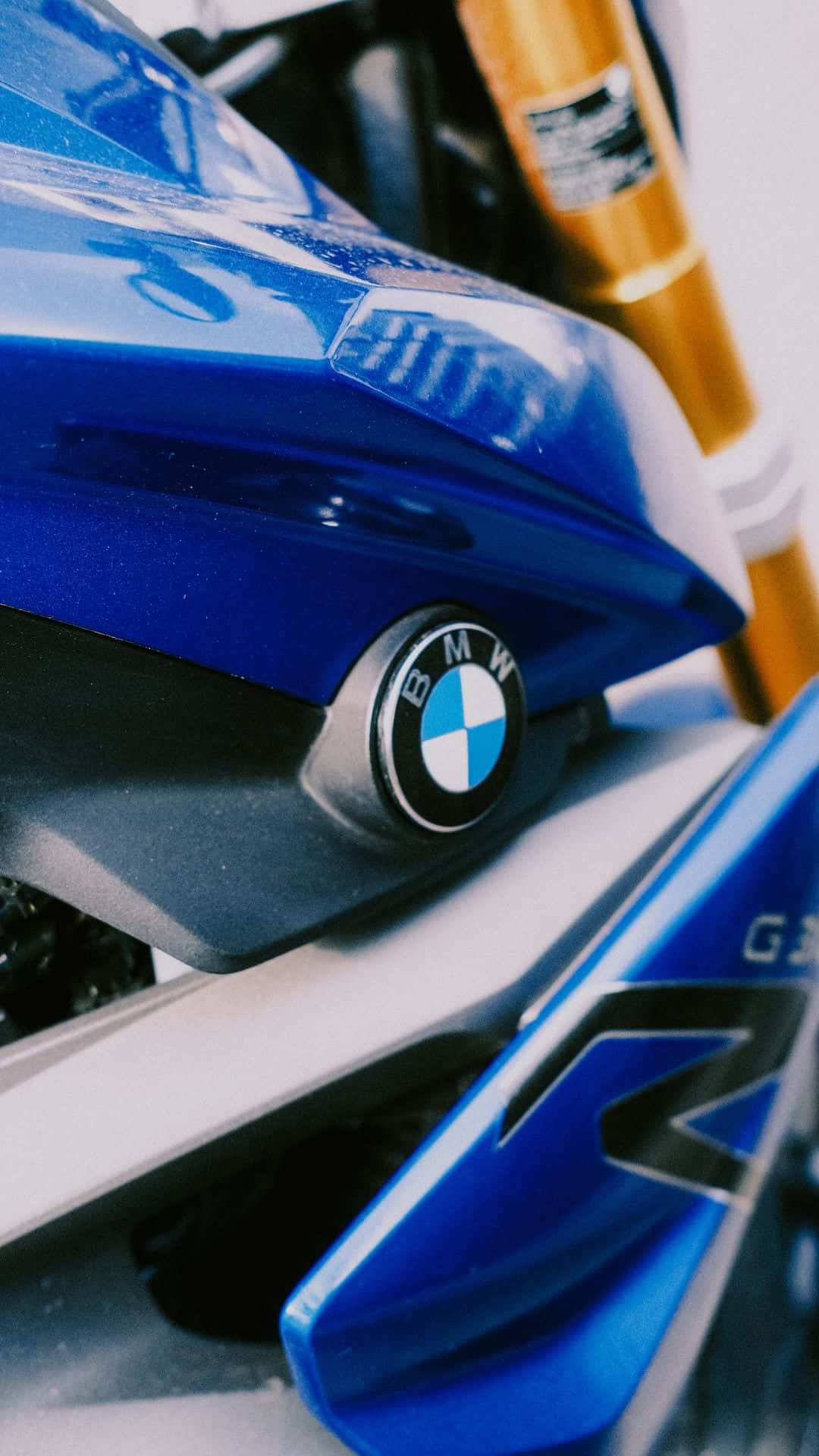 Android Bmw 桌布 壁紙 — 特寫一輛光澤藍色BMW機車，配金色前叉和銳利線條，在明亮光線下。