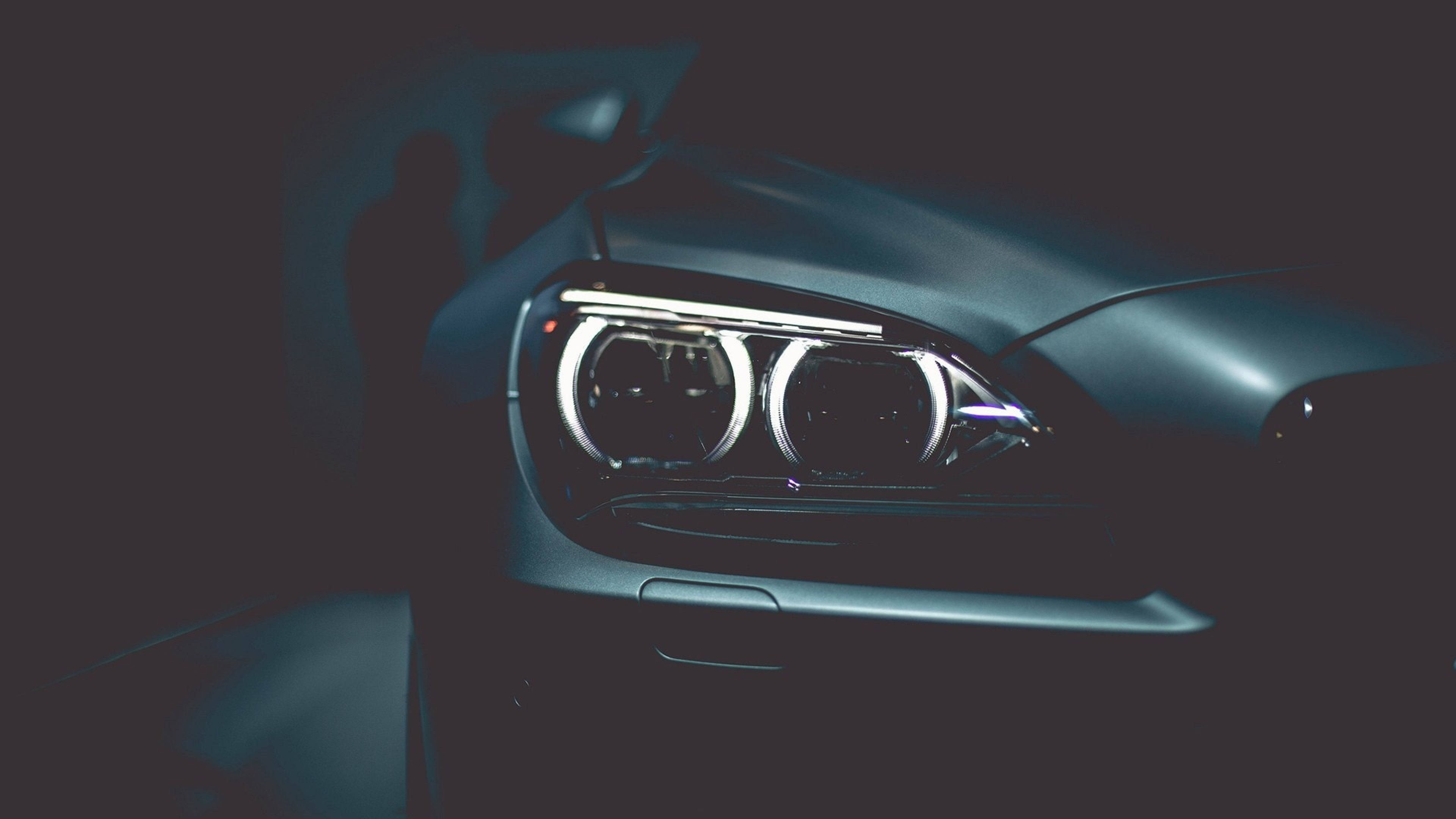 4K BMW 壁紙 桌布 壁紙 — 特寫一輛時尚汽車在昏暗燈光下發光的車頭燈，投射出戲劇性的陰影。