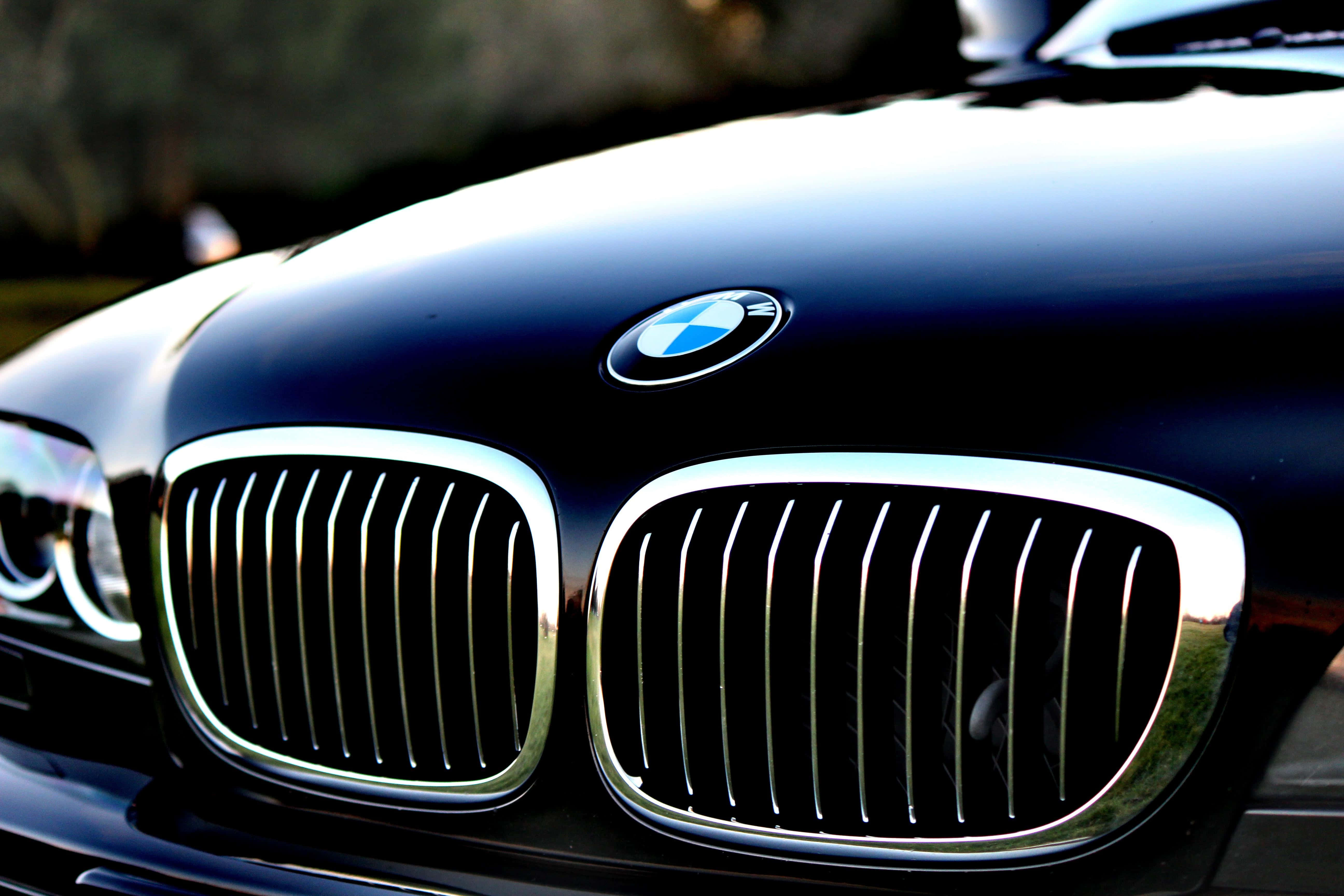 BMW 動圖 桌布 壁紙 — 特寫一輛時尚黑色寶馬汽車引擎蓋，在明亮陽光下展示標誌性的腎形格柵和標誌。