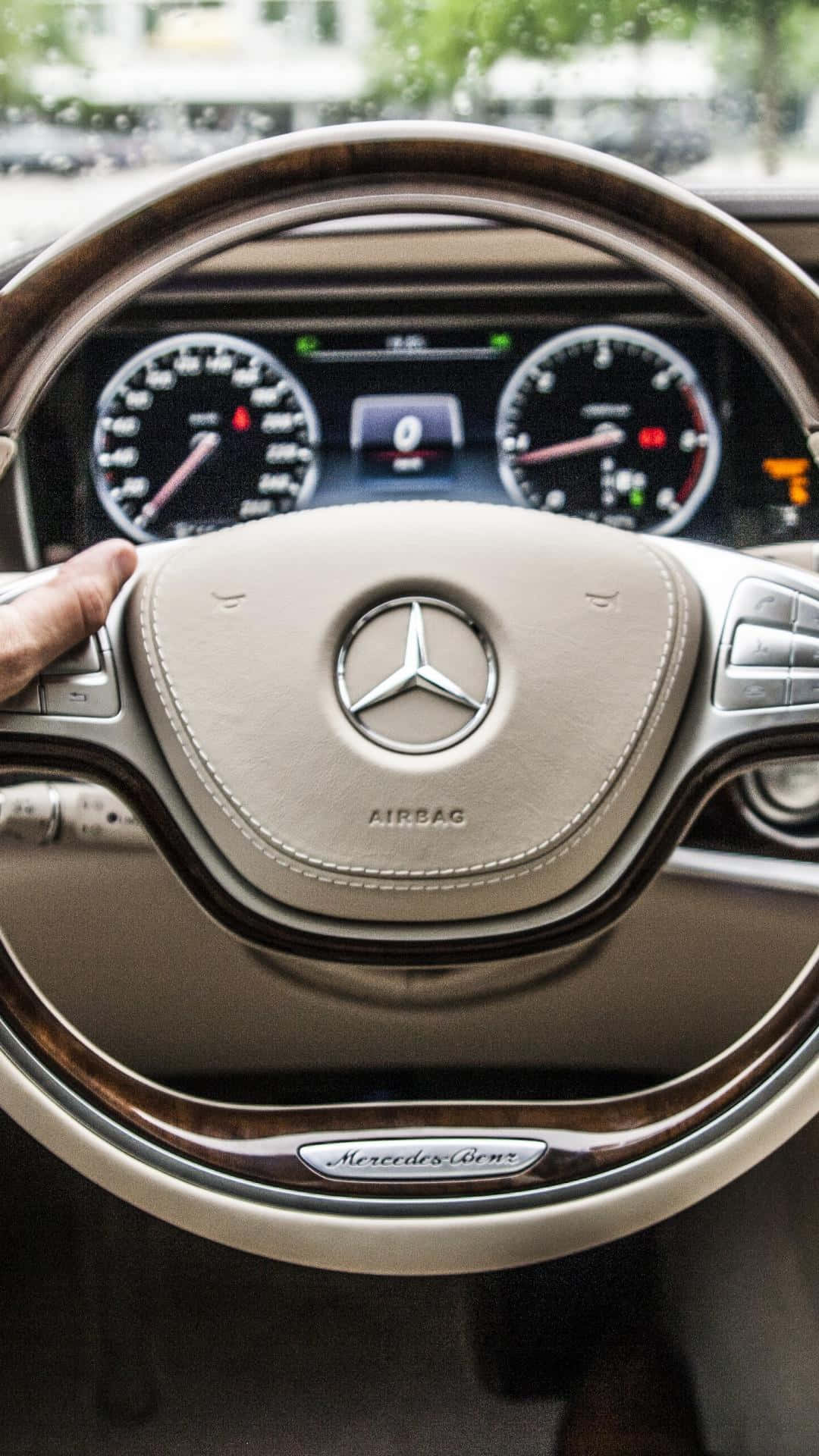 汽車 桌布 壁紙 — 特寫一隻手抓握豪華 Mercedes-Benz 方向盤，帶有木質飾邊和發光的儀表板儀表。