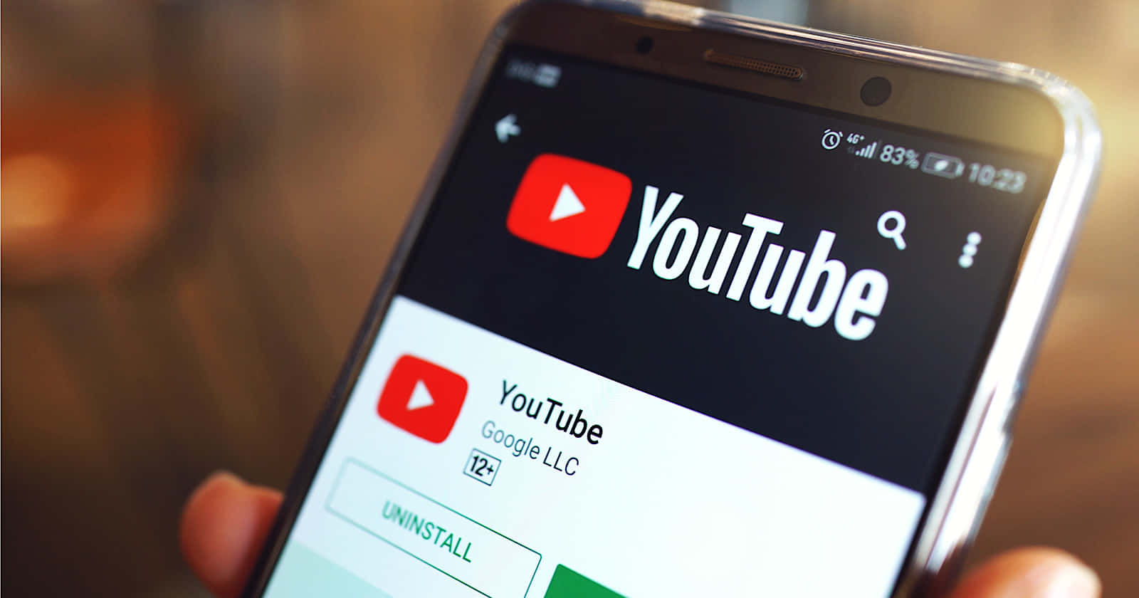YouTube 桌布 壁紙 — 特寫一隻手拿著智慧型手機，顯示 YouTube 應用程式商店頁面，應用程式圖示和解除安裝按鈕可見。