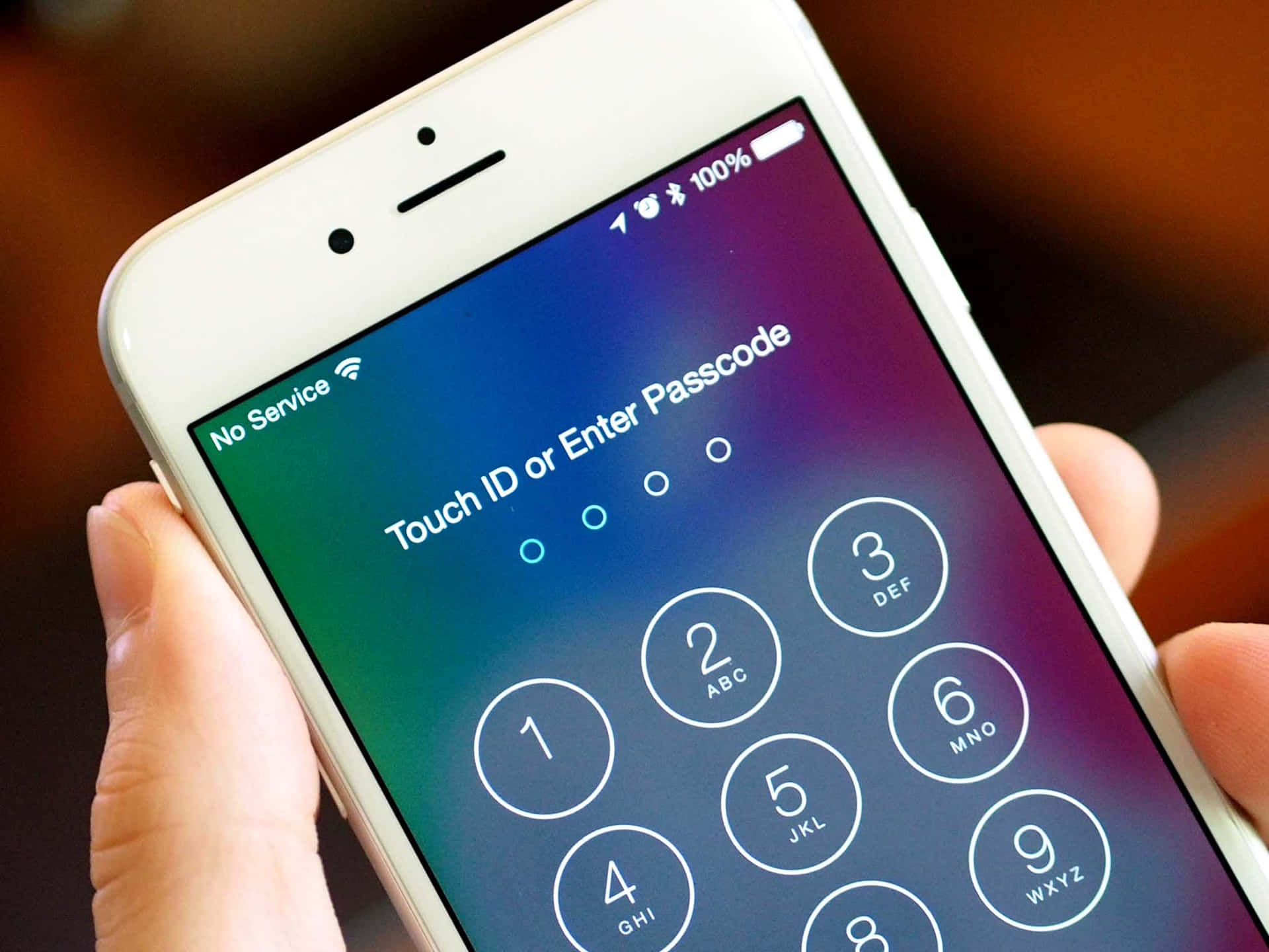 Touch Id 桌布 壁紙 — 特寫一隻手拿著白色iPhone，顯示密碼解鎖畫面，背景為漸層色。