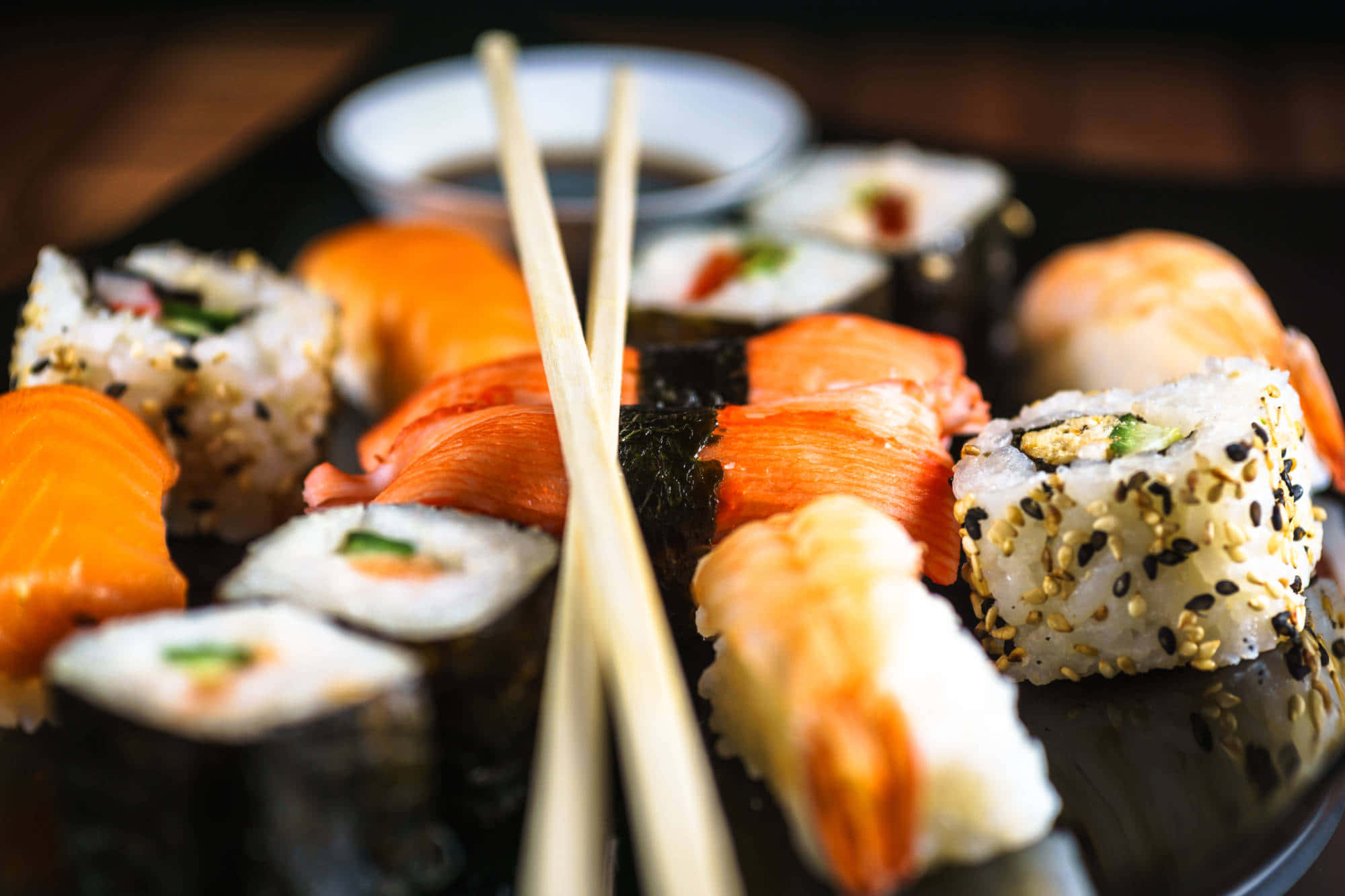 Sushi 桌布 壁紙 — 特寫各種壽司卷和握壽司，筷子放在深色盤子上。