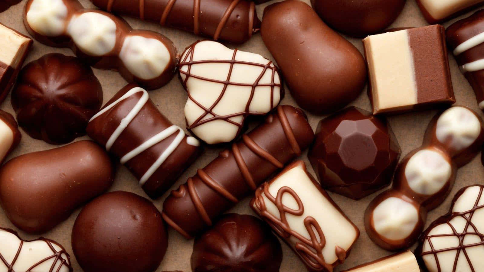 Chocolate 桌布 壁紙 — 特寫各種巧克力，上面有白巧克力和黑巧克力淋醬和形狀，放在棕色表面上。