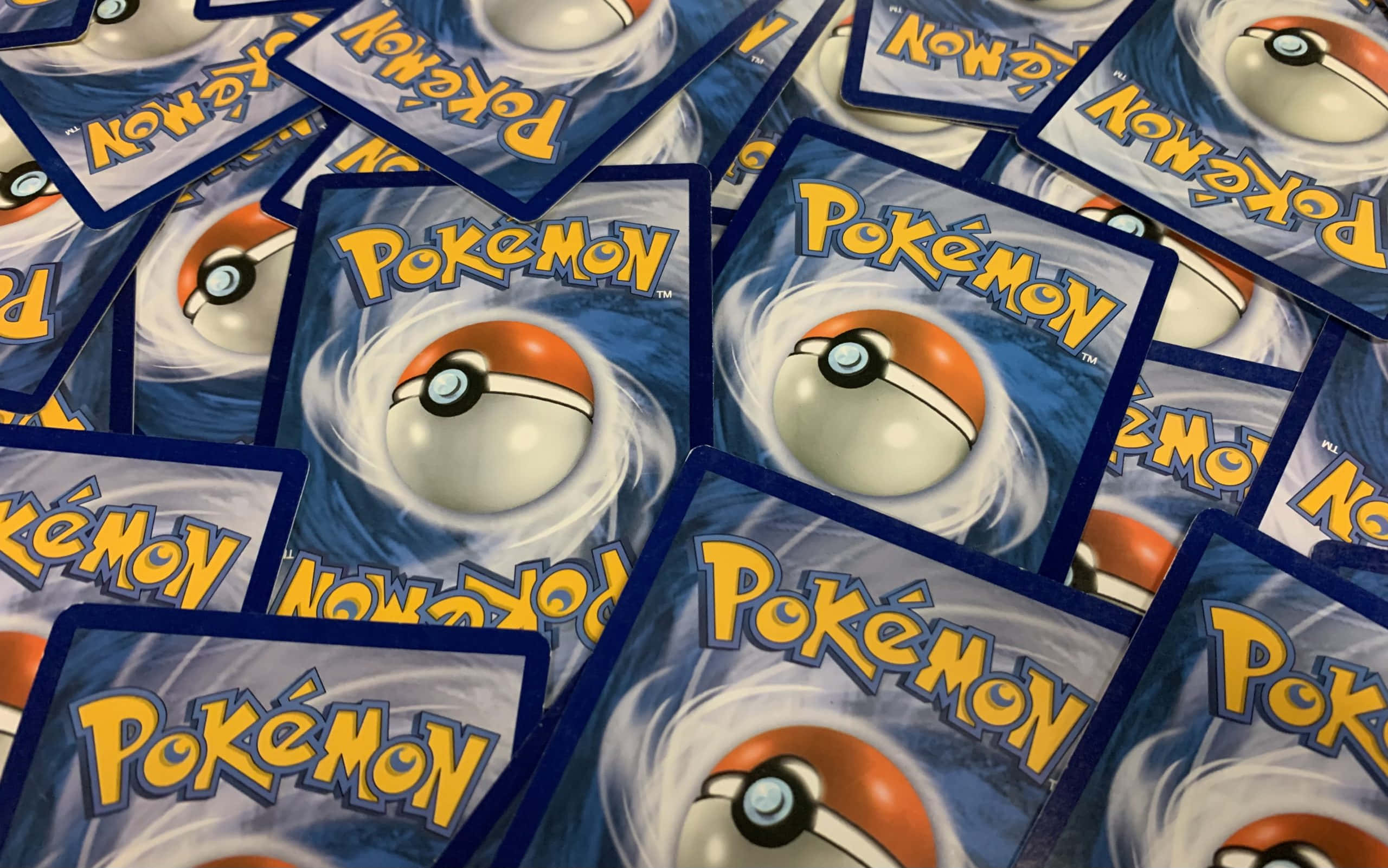 Pokemon Card 桌布 壁紙 — 特寫散落的寶可夢集換式卡牌，上面有標誌性的寶可夢球標誌，背景是旋轉的藍色。
