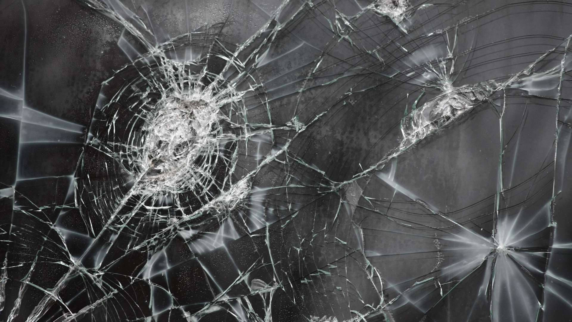Broken Computer Screen 桌布 壁紙 — 特寫破碎玻璃，裂紋從撞擊點向四周擴散，背景為深色。
