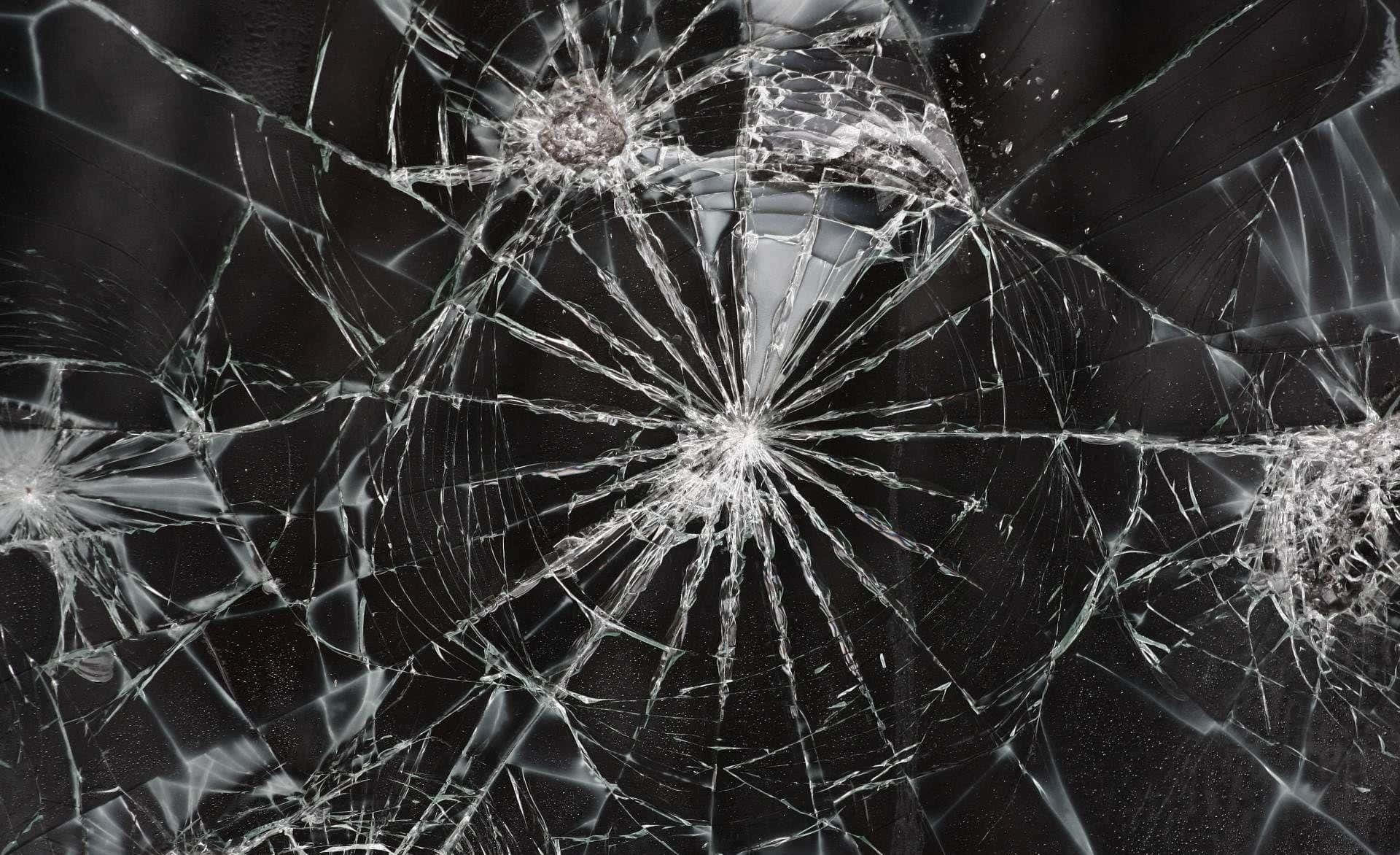 cracked 桌布 壁紙 — 特寫破碎玻璃，裂紋從撞擊點複雜地輻射開來，背景為深色。