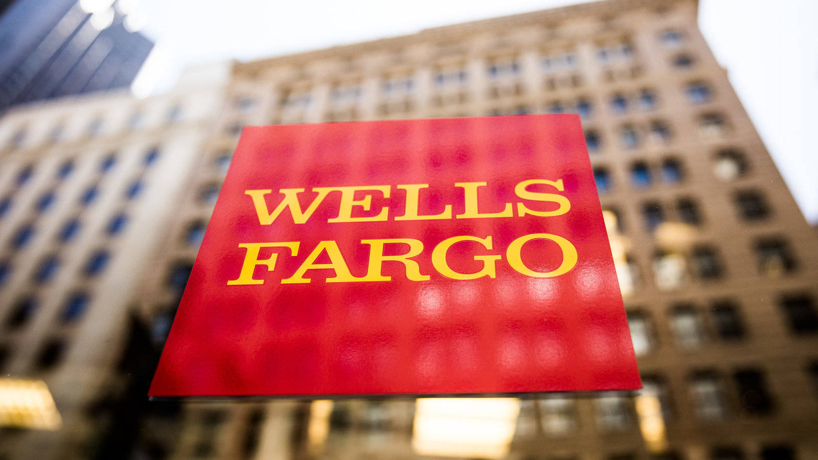 Building 桌布 壁紙 — 特寫紅色 Wells Fargo 標誌，黃色字體，背景為模糊的城市建築。