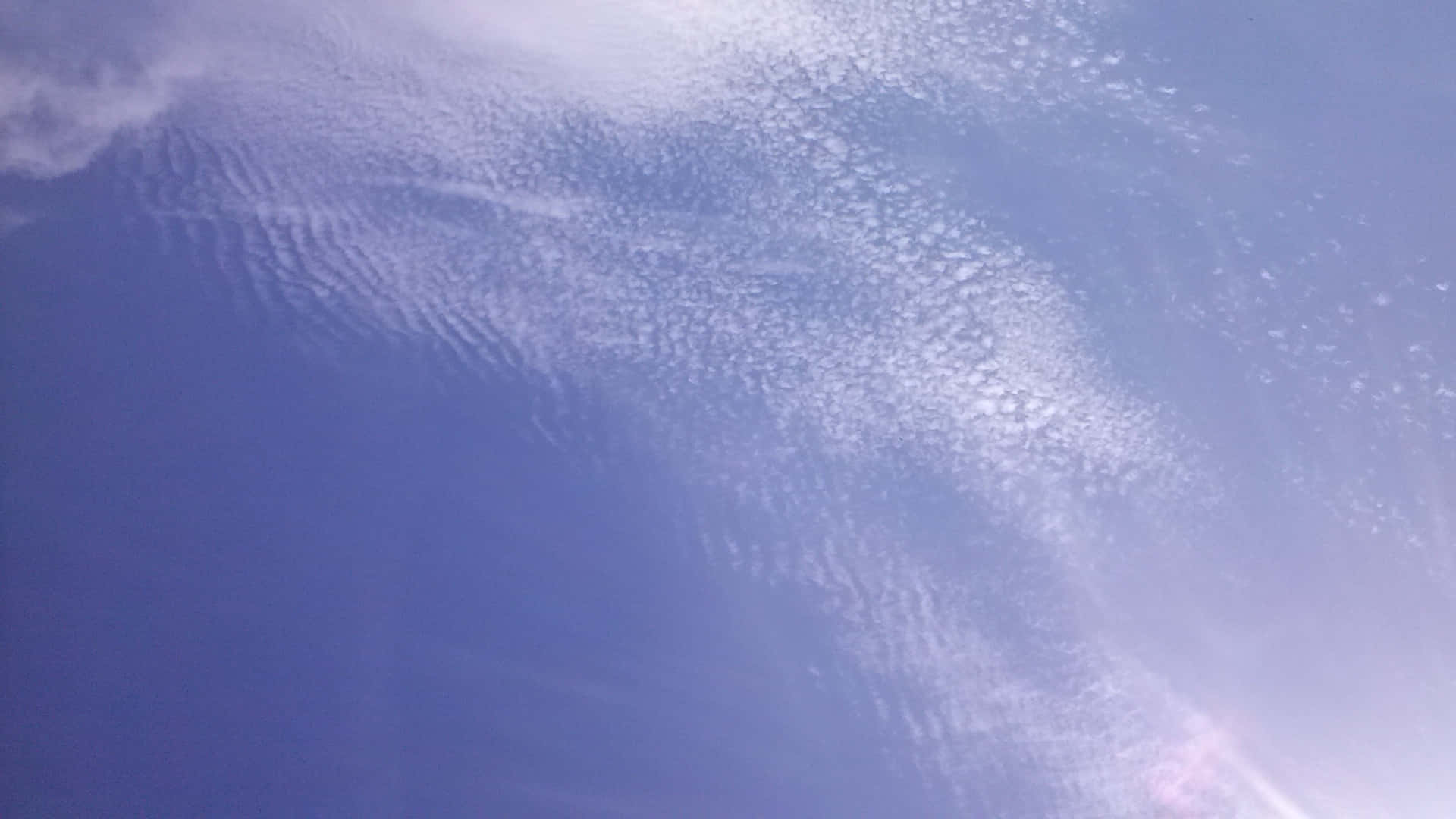SKY-12 壁紙 — 特寫紋理藍天，帶有縷縷白雲和角落柔和的太陽耀斑。